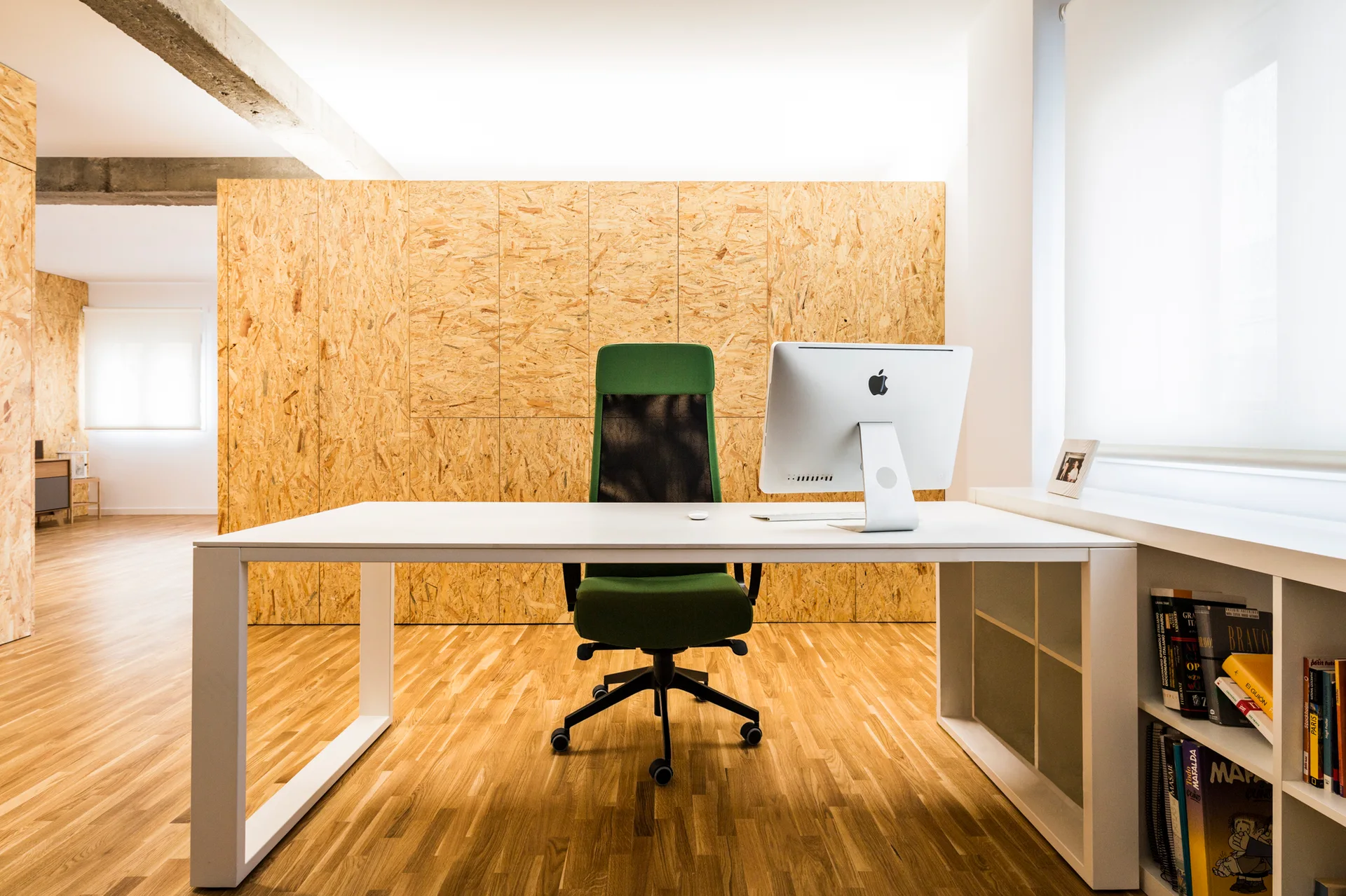 A minimalist home office featuring a white desk, a green chair, and a back wall covered in oriented strand board wood paneling.
