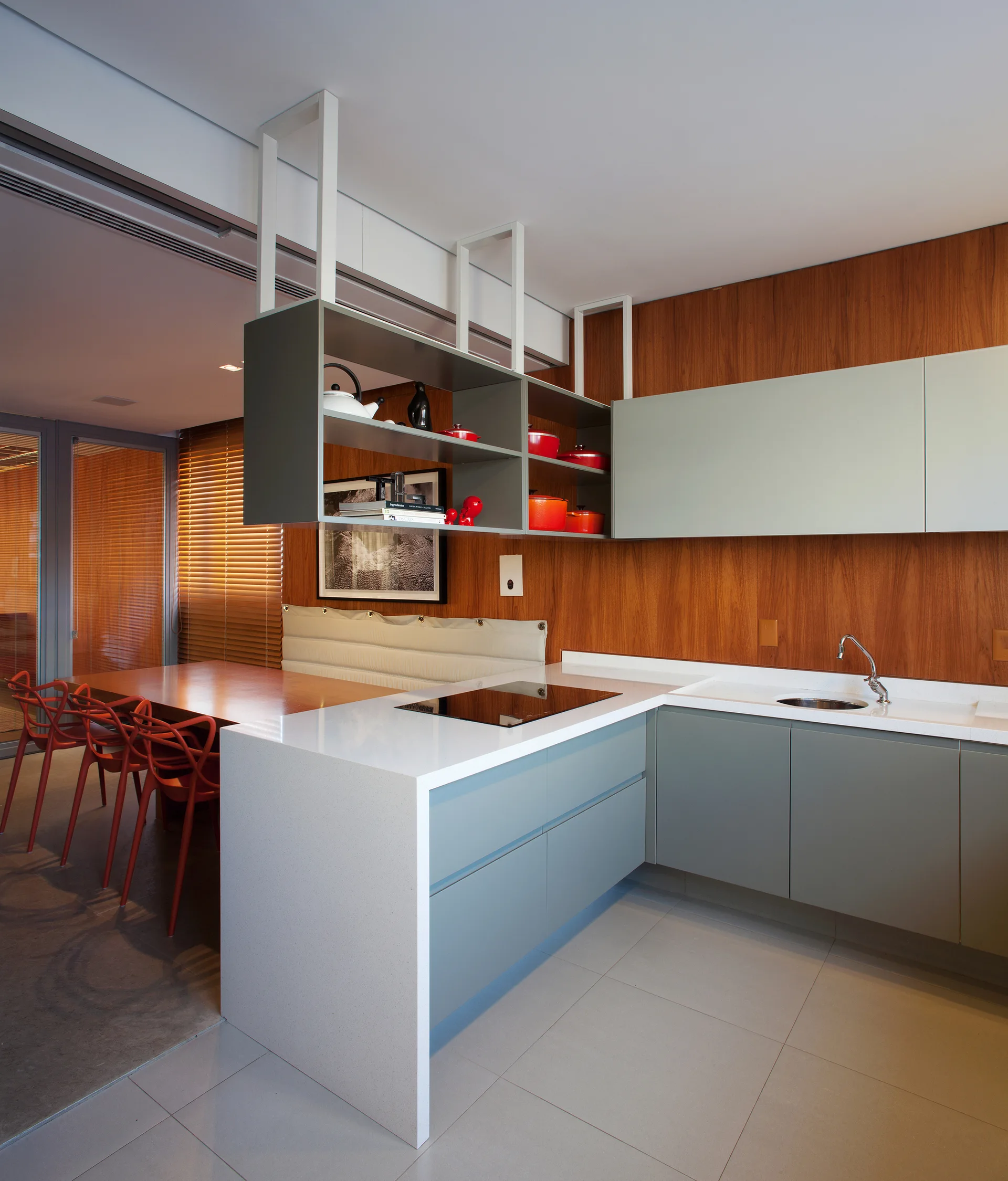 A modern kitchen features grey cabinetry, white waterfall countertops, wood-paneled walls, and a grey open shelf suspended from the ceiling.
