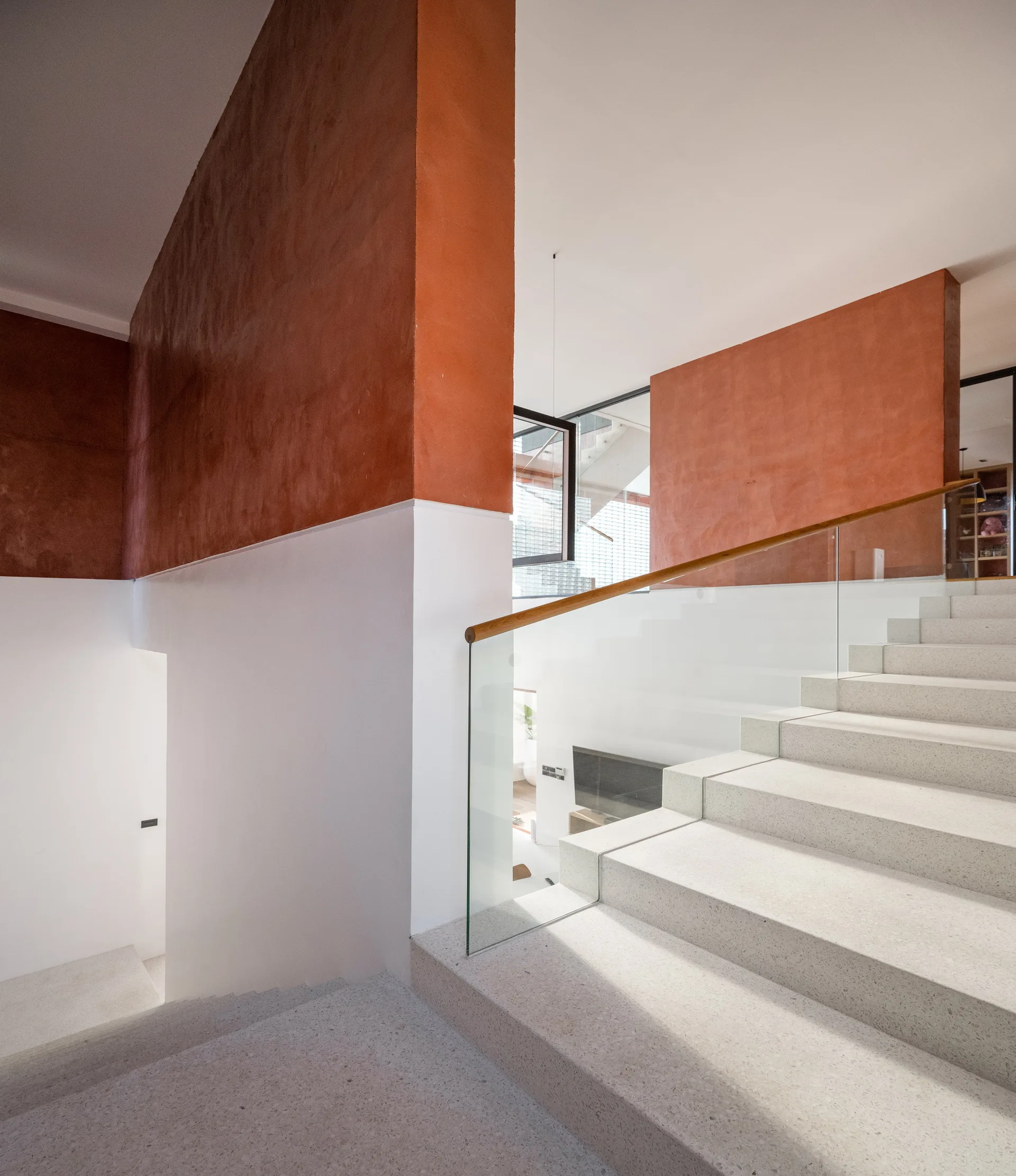 A modern stone staircase with a glass railing climbs past a two-tone wall painted in terracotta and white.