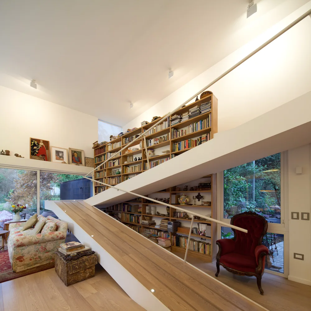 A light wood ramp staircase ascends diagonally across a tall, fully stocked wooden bookshelf in a white-walled living room.