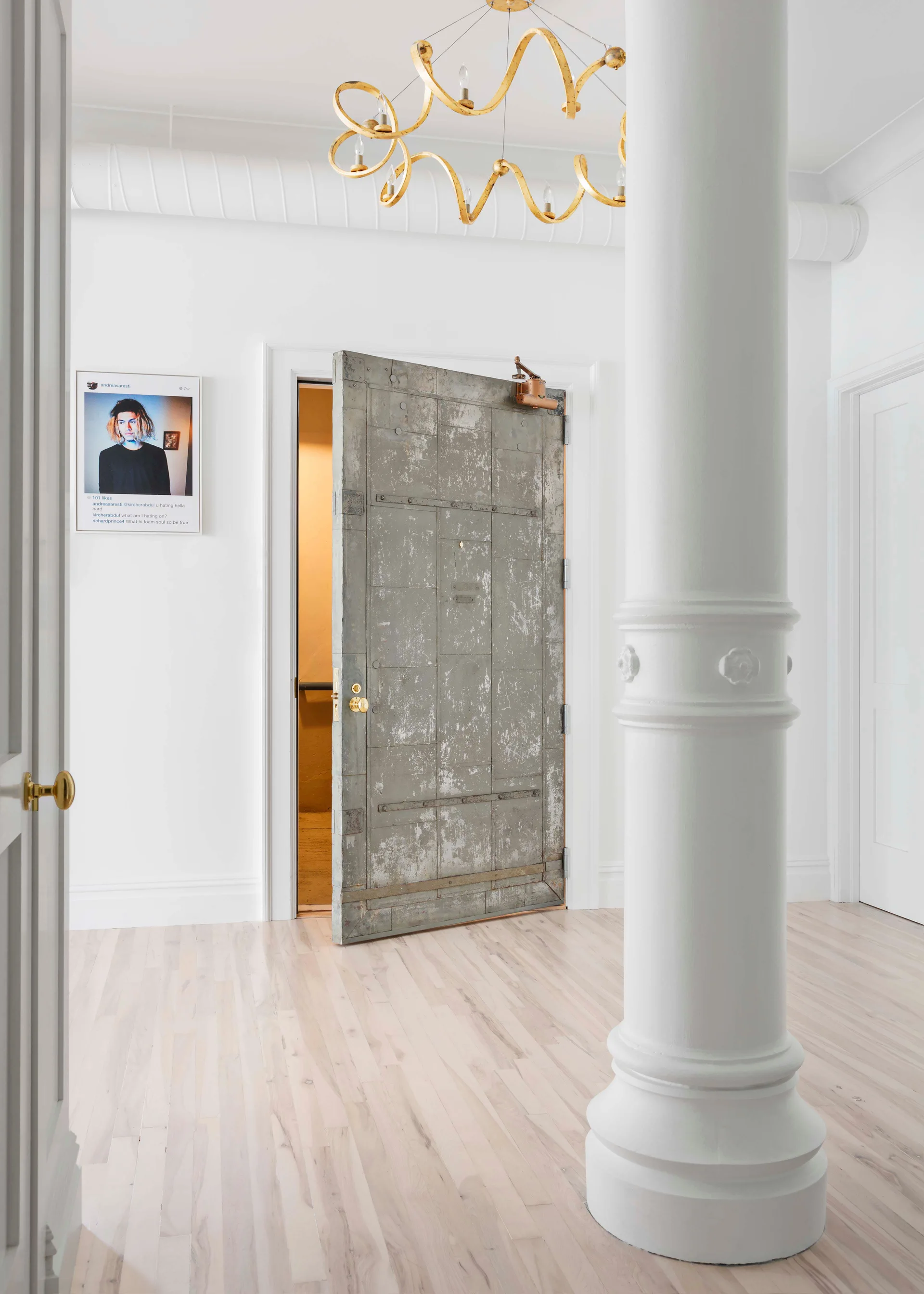 A bright entryway features light wood flooring, a white structural column, and an open distressed metal industrial door.