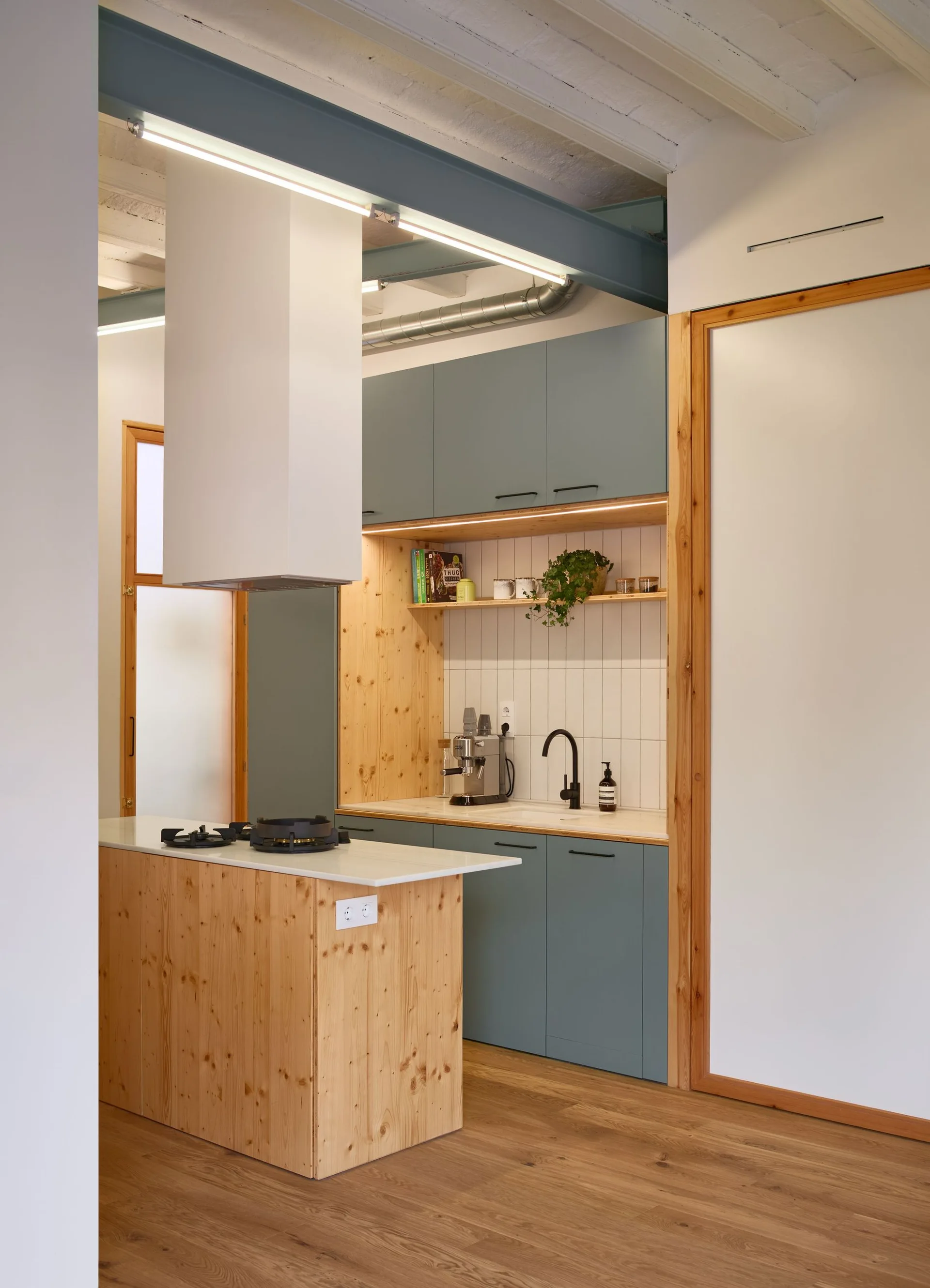 A modern kitchen featuring sage green cabinets, a natural pine kitchen island with a white countertop, and vertical white backsplash tiles.