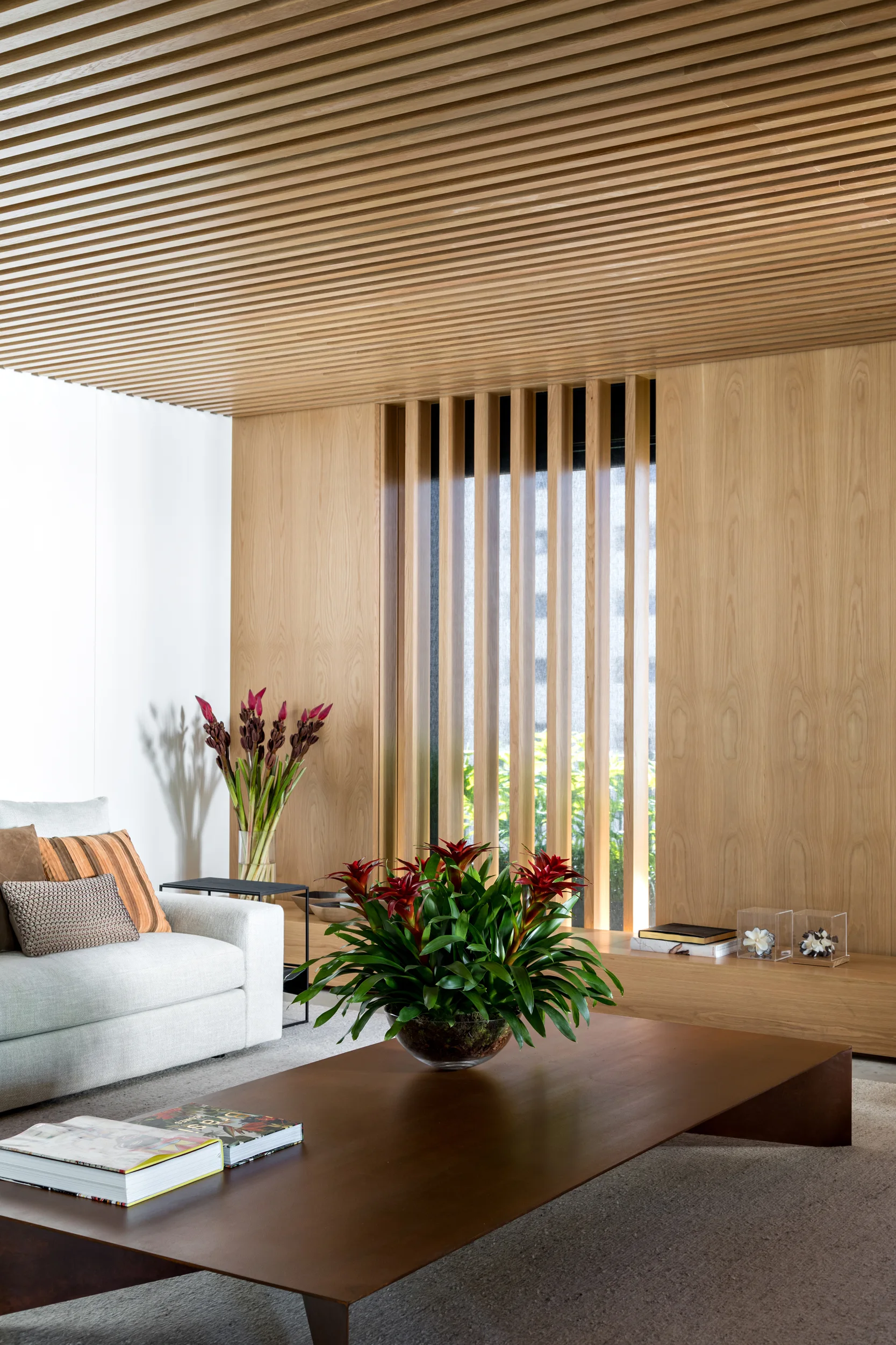 A light grey sofa and a low wooden coffee table in a living room featuring a slatted wood ceiling and matching wood paneled walls.