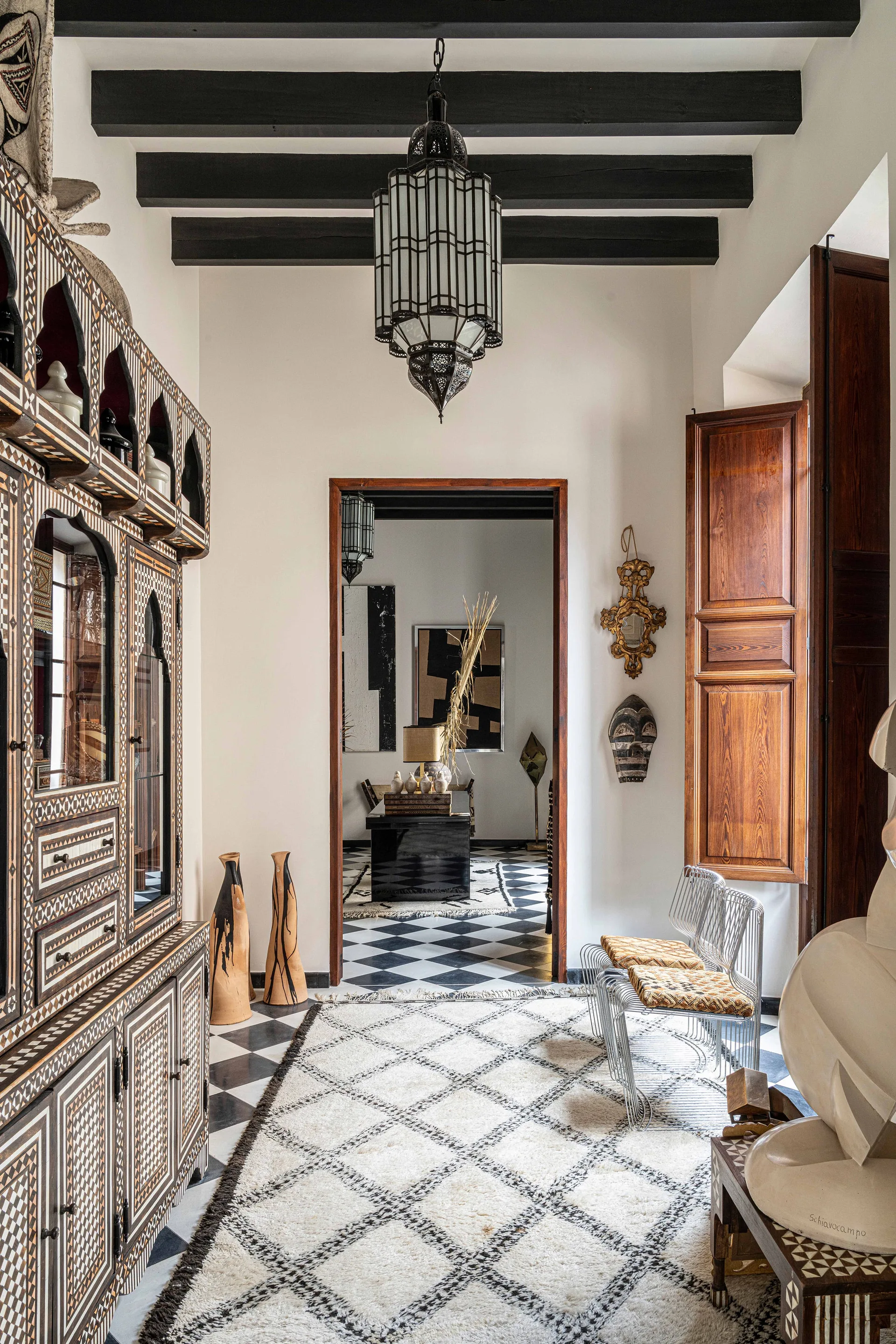 A high-contrast entryway features a large wood inlay cabinet, black and white checkerboard flooring, exposed ceiling beams, and a hanging metal lantern.