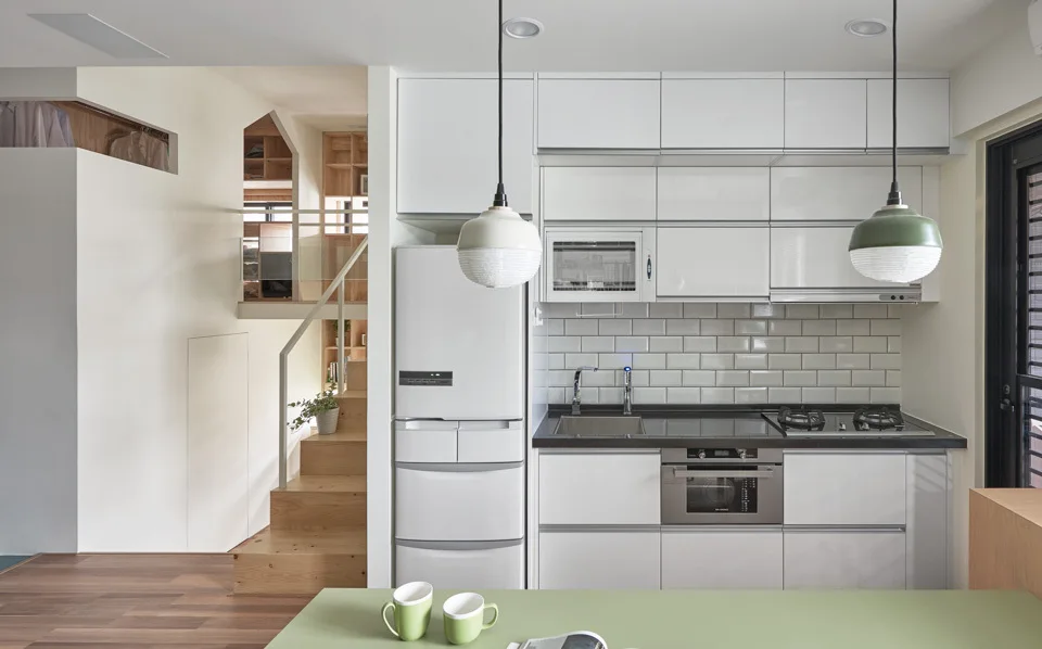 A modern kitchen featuring glossy white cabinets, a subway tile backsplash, and a light wood staircase in the background.