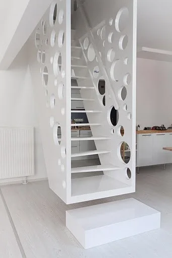 A minimalist white floating staircase features an enclosure panel with circular cutouts of various sizes.