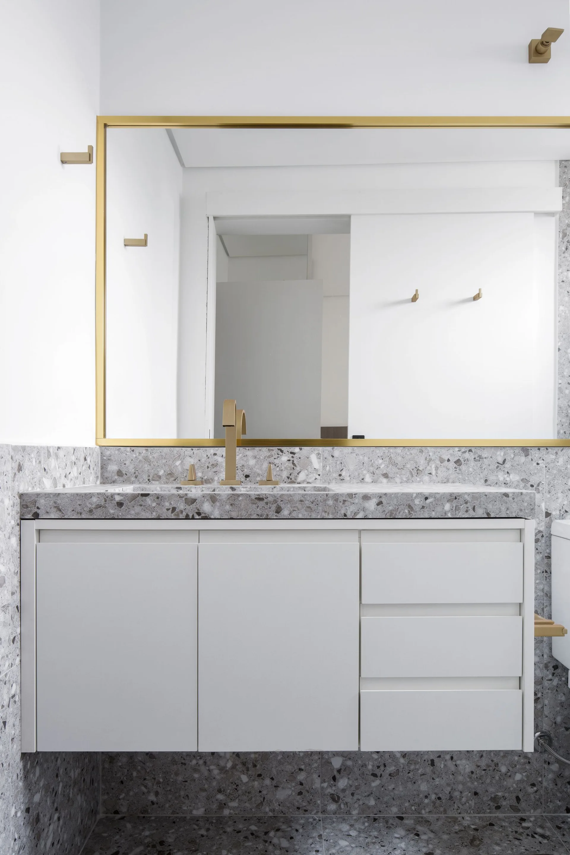 A white floating bathroom vanity features a grey terrazzo countertop, matching terrazzo backsplash, and a gold-framed mirror on the wall above.