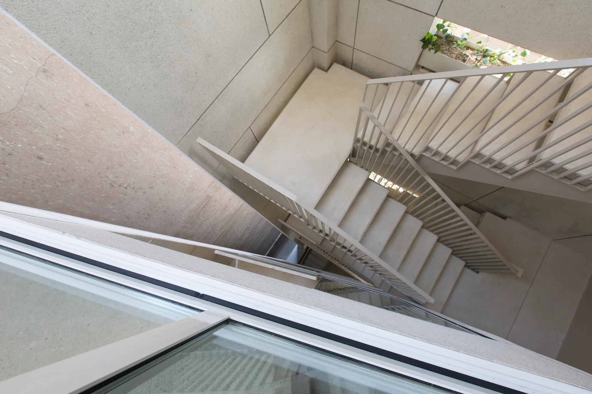 A high-angle view of a minimalist off-white concrete staircase with thin metal railings and large wall panels.