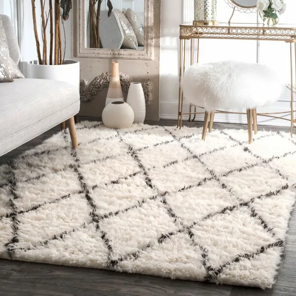 A plush cream shag rug with a dark diamond pattern sits on dark wood flooring next to a gold console table and fluffy white stool.