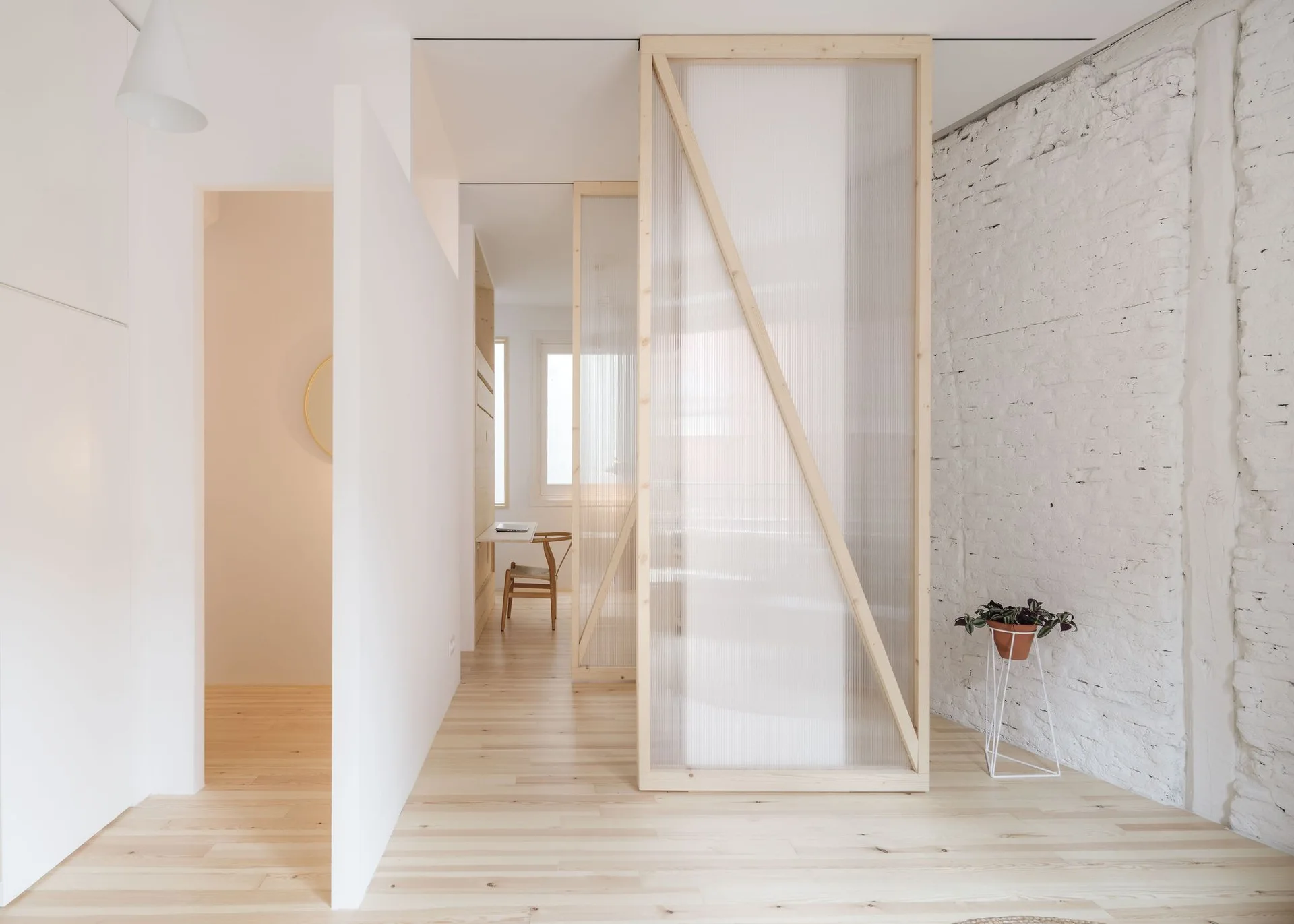 A minimalist hallway features light wood floors, a painted brick wall, and a wood-framed translucent polycarbonate room divider.