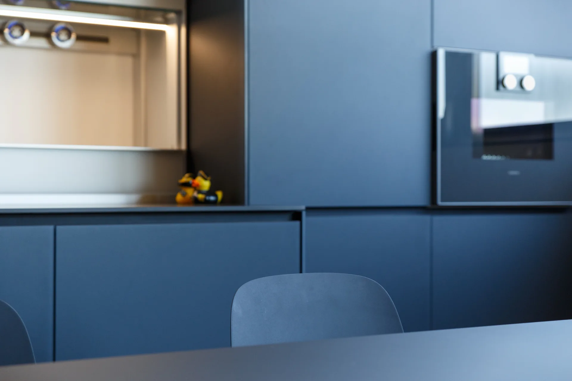 Modern kitchen featuring matte dark blue seamless cabinetry, an integrated oven, and a built-in illuminated counter alcove.