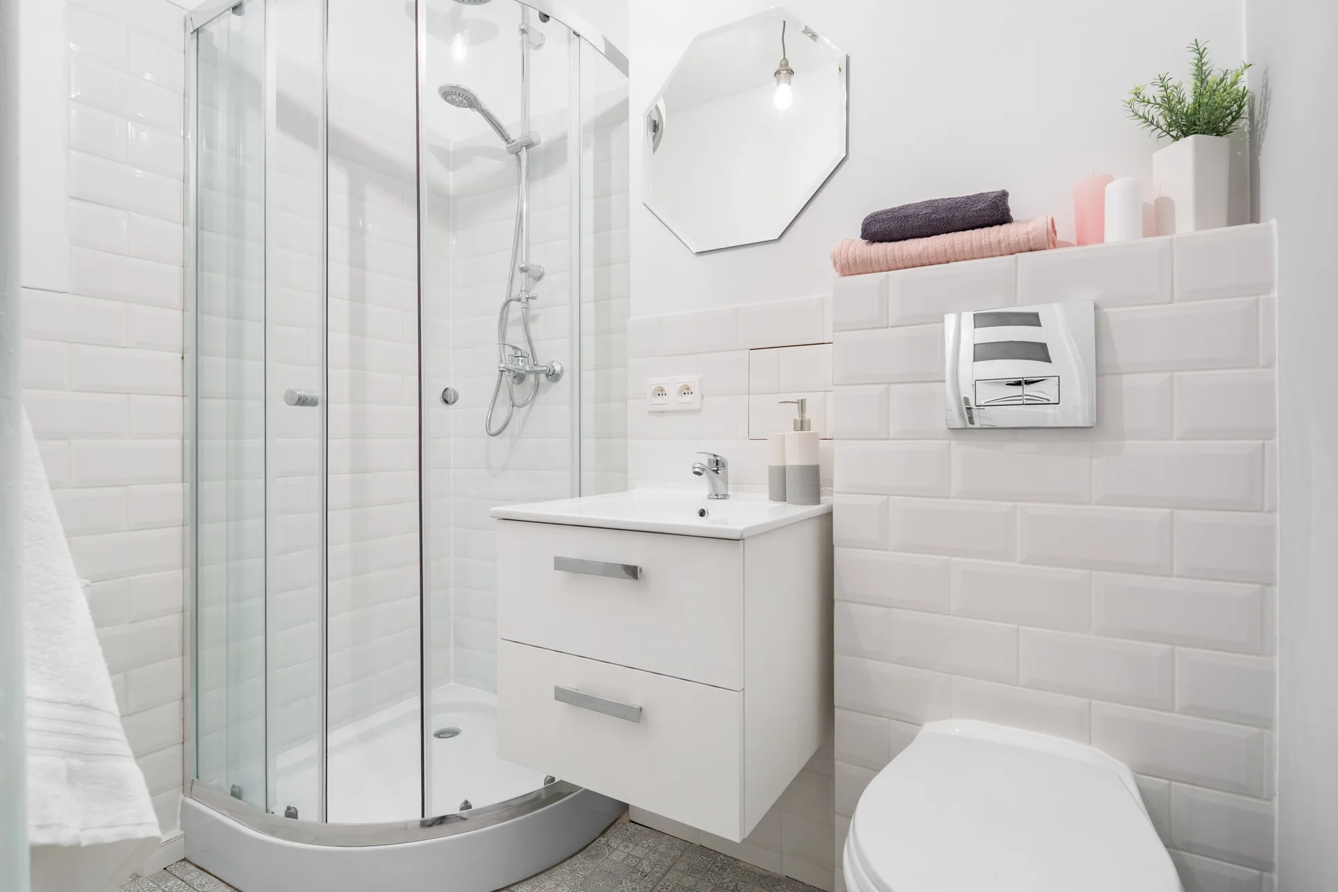 A compact white bathroom with a curved glass corner shower, a wall-mounted sink vanity, and white subway tiled walls.