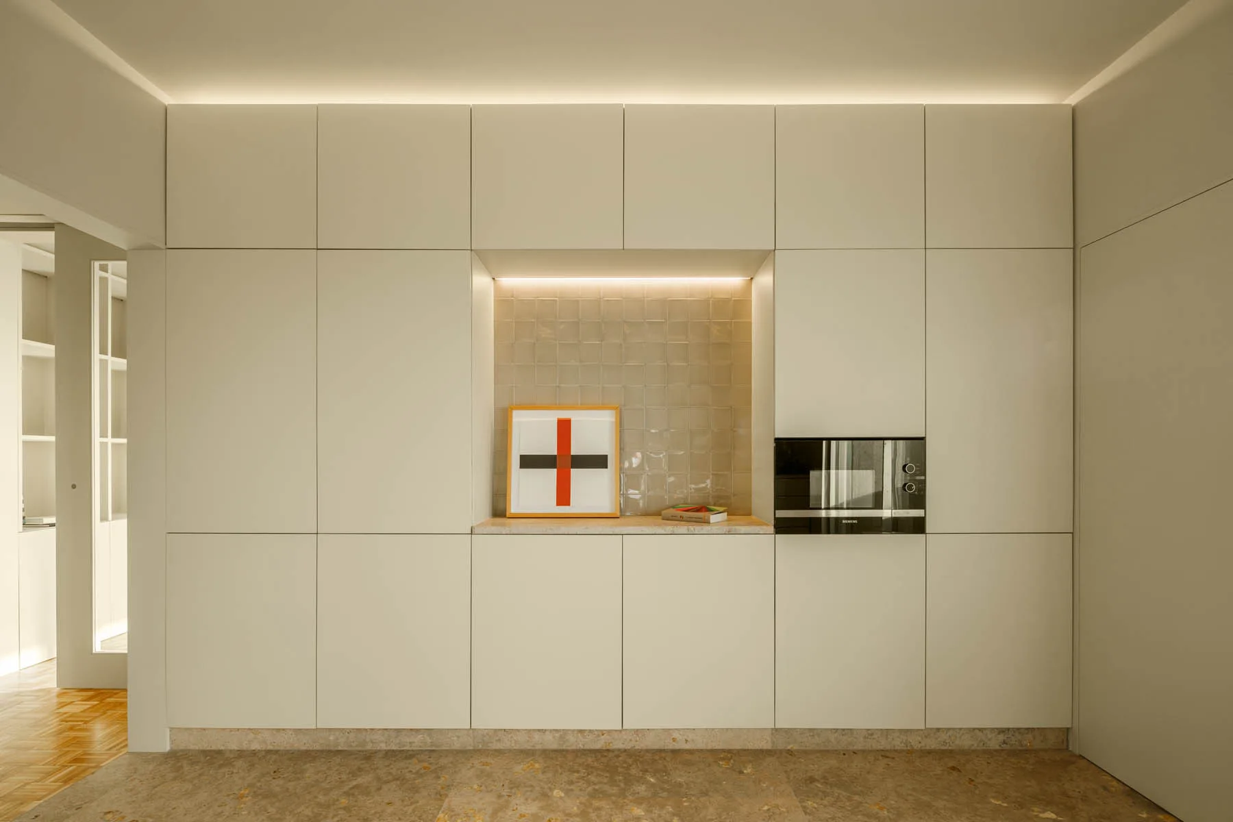 A seamless off-white built-in kitchen cabinet wall featuring a recessed tiled niche with artwork and an integrated black microwave.