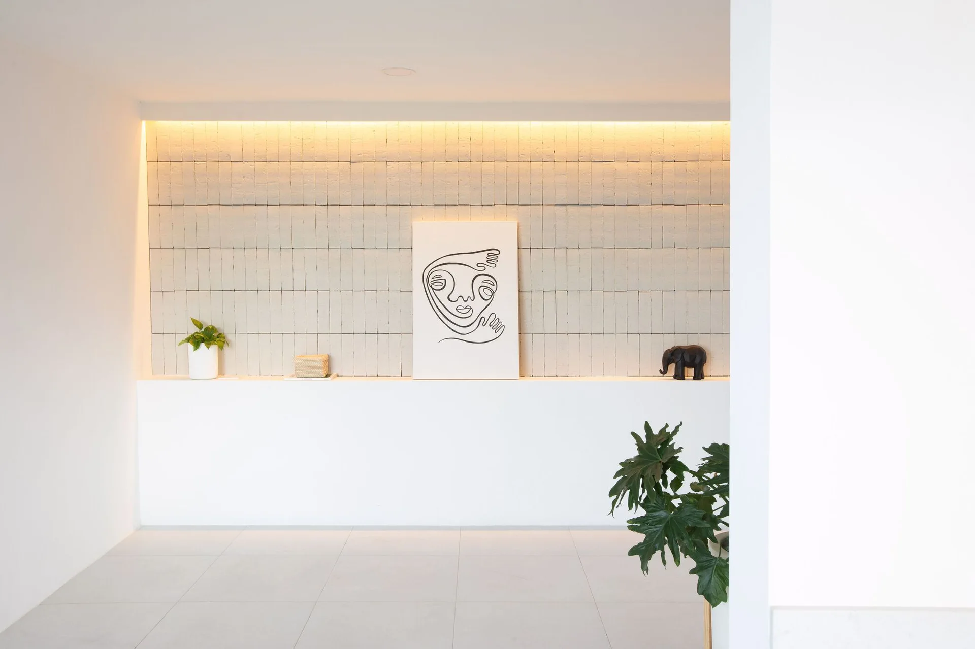 A minimalist display ledge features a grid-tiled accent wall illuminated by warm cove lighting and decorated with line art and small objects.