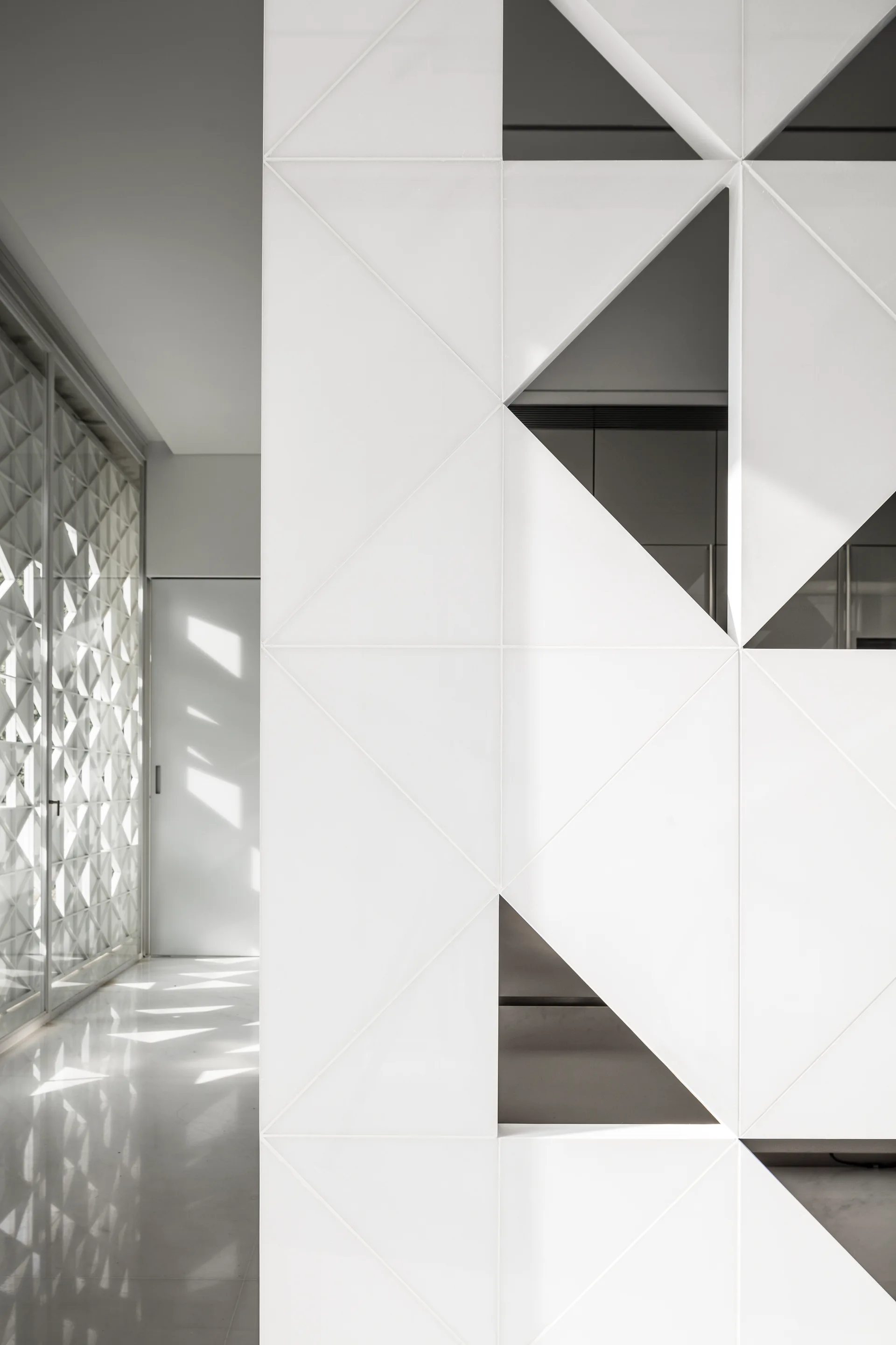 A bright white interior hallway features a modern geometric partition wall with triangular cutouts and a matching latticework screen.