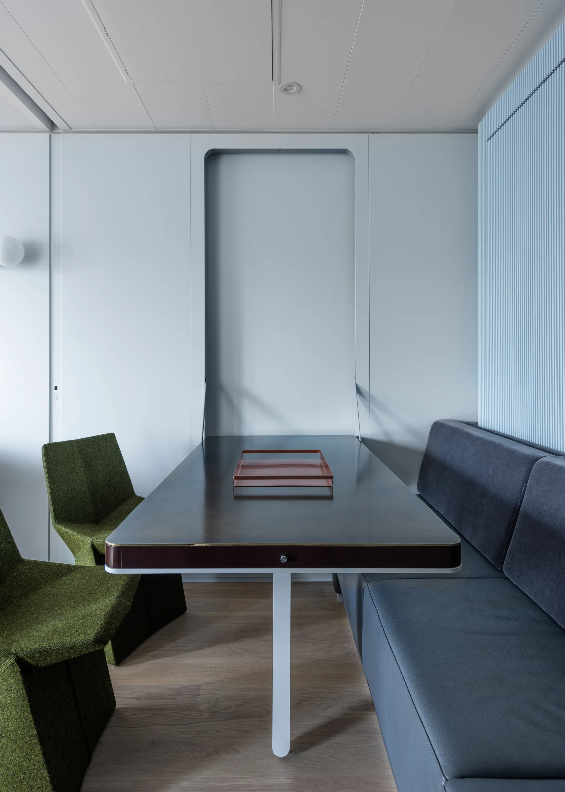 A modern dining nook features a dark rectangular table, green textured chairs, a built-in gray bench, and a light blue fluted accent wall.