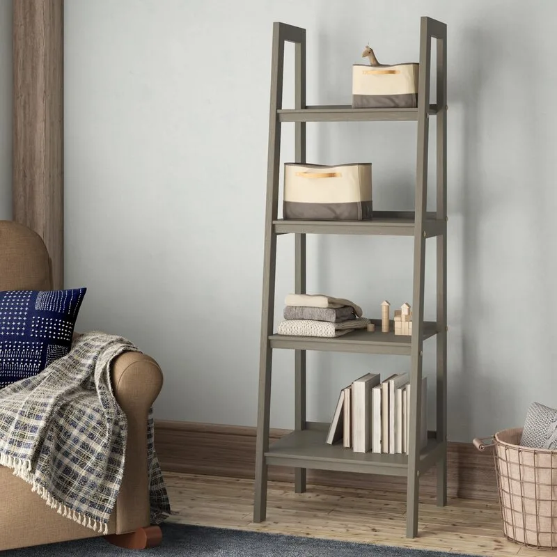 A gray wooden ladder shelf stands against a light gray wall next to an armchair with a plaid blanket.