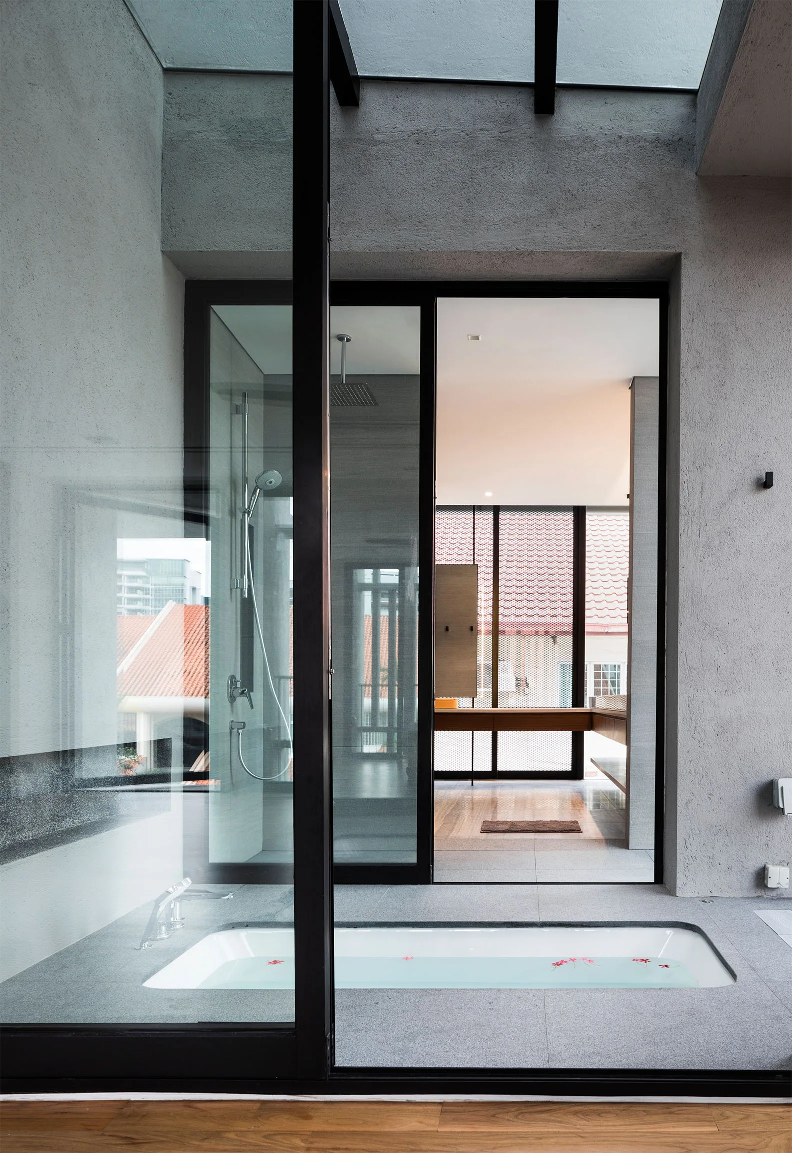 A minimalist gray bathroom features a sunken bathtub in a stone floor, glass sliding doors, and a skylight.