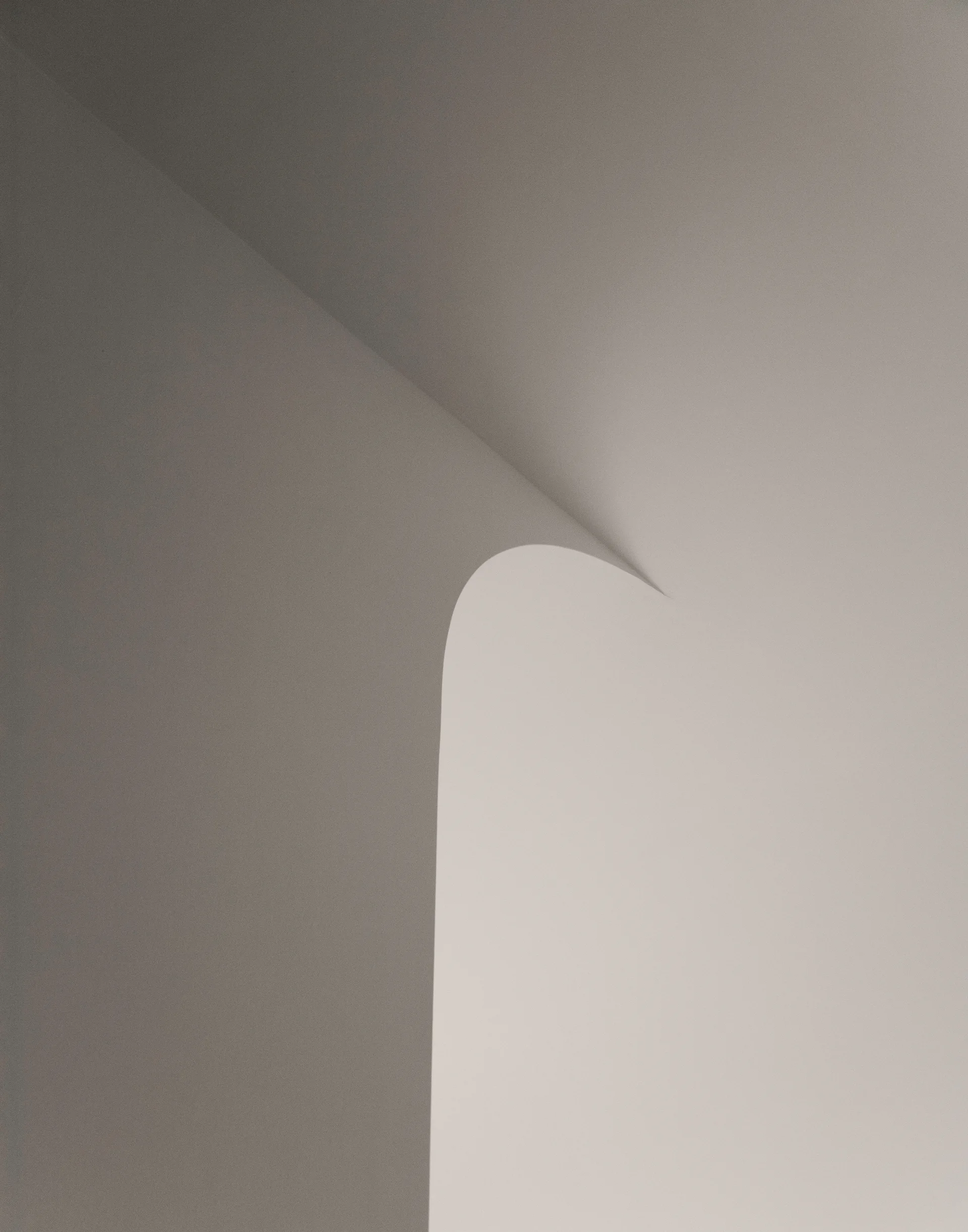 A close-up of a clean minimalist interior showing a smooth plaster wall with a curved archway corner casting soft shadows.