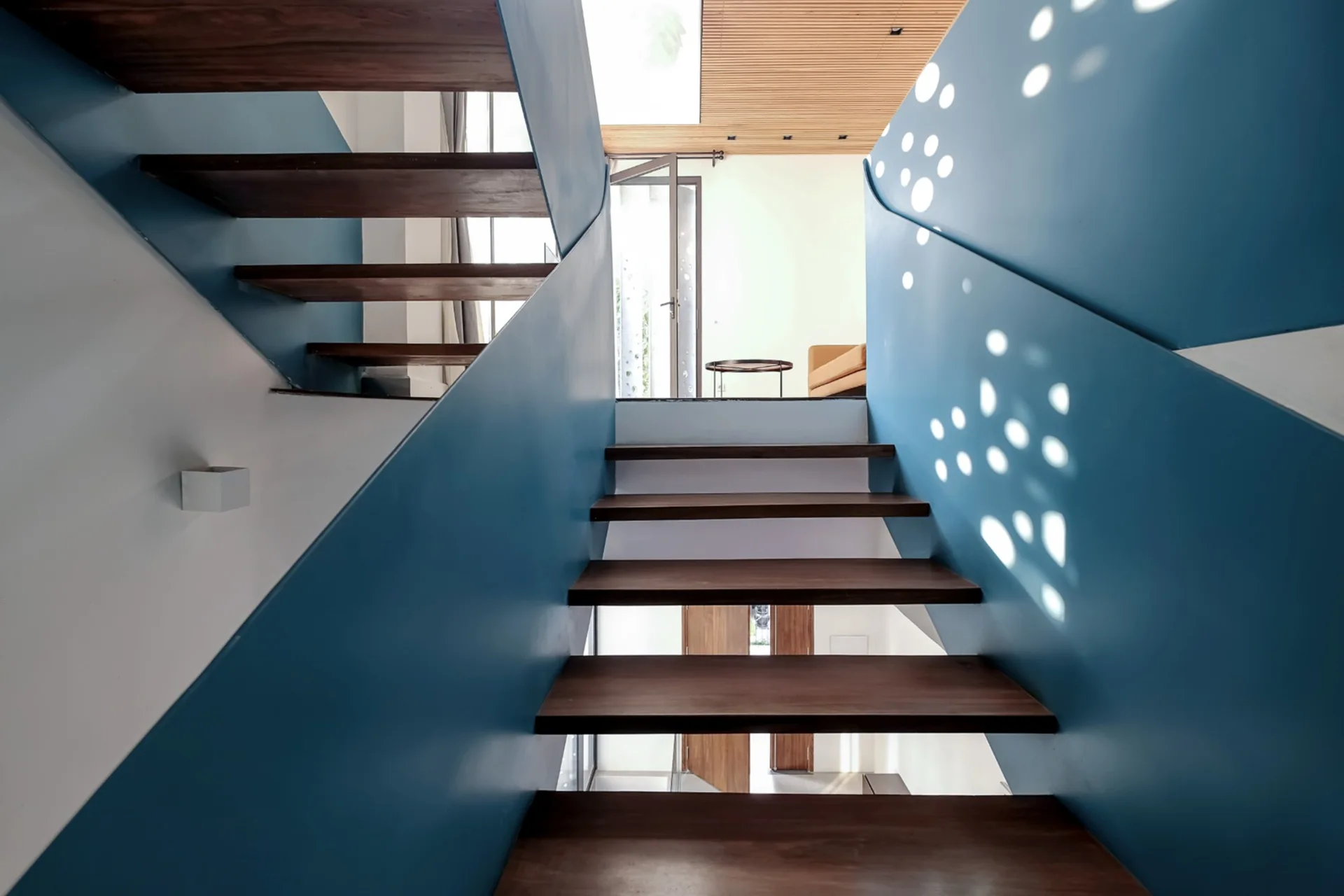 A modern staircase features dark wood treads set between solid blue painted balustrades, with circular perforated cutouts on one side.
