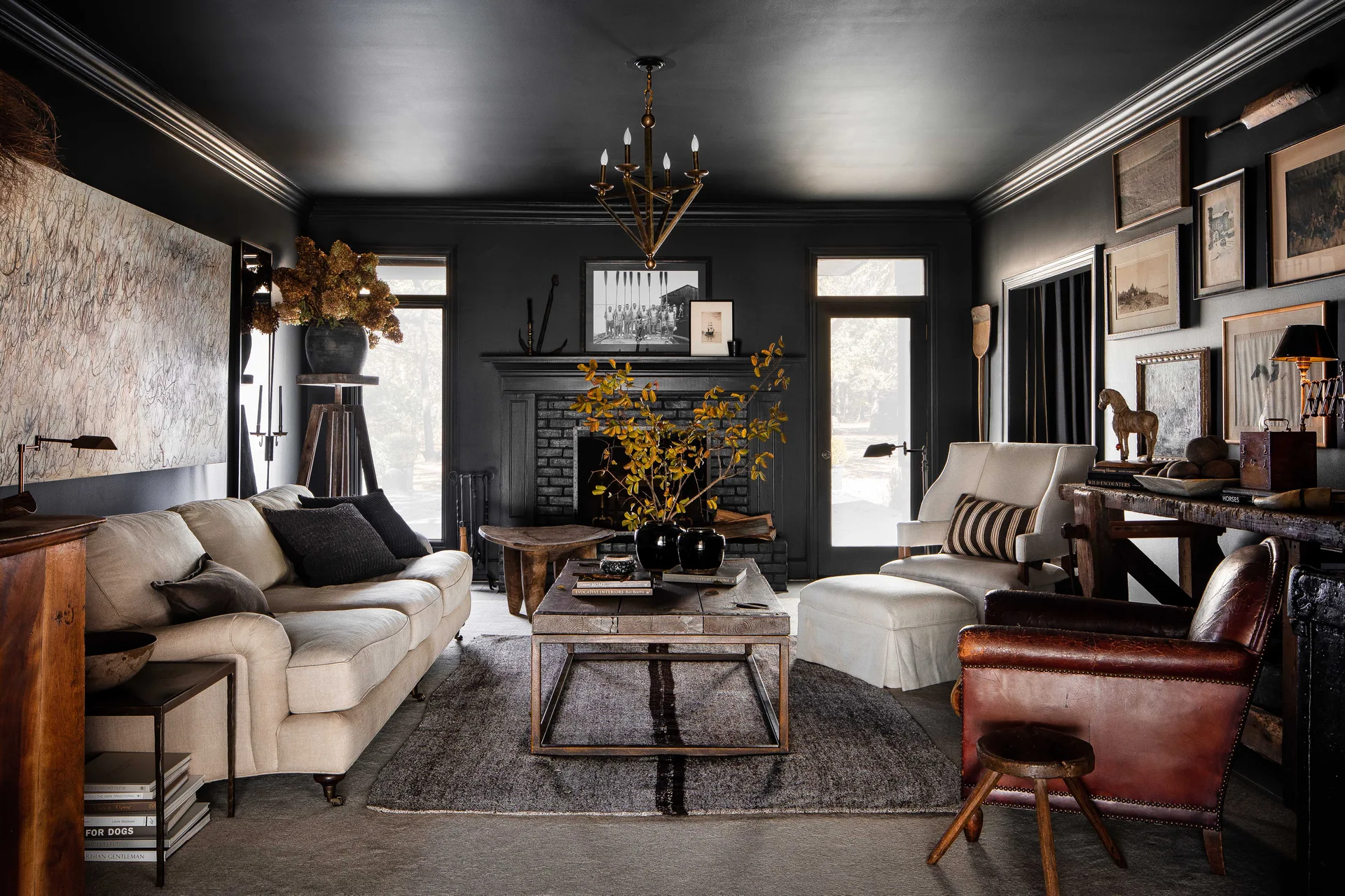 A moody living room featuring charcoal walls and ceiling, a black brick fireplace, a cream sofa, and a leather armchair on a textured rug.