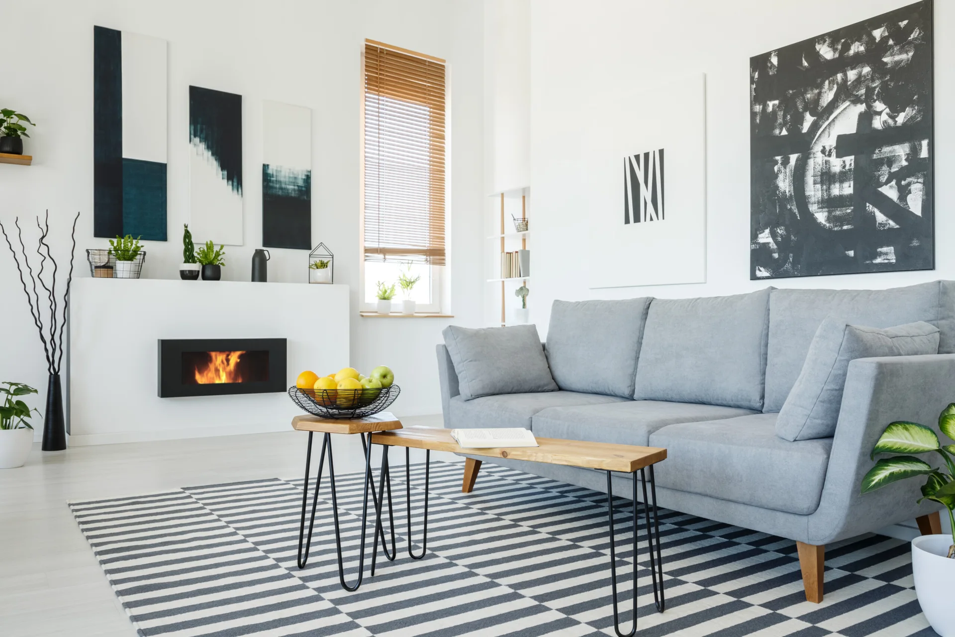 A modern Scandinavian living room features a grey upholstered sofa, wood nested coffee tables, a striped geometric rug, and a sleek inset fireplace.