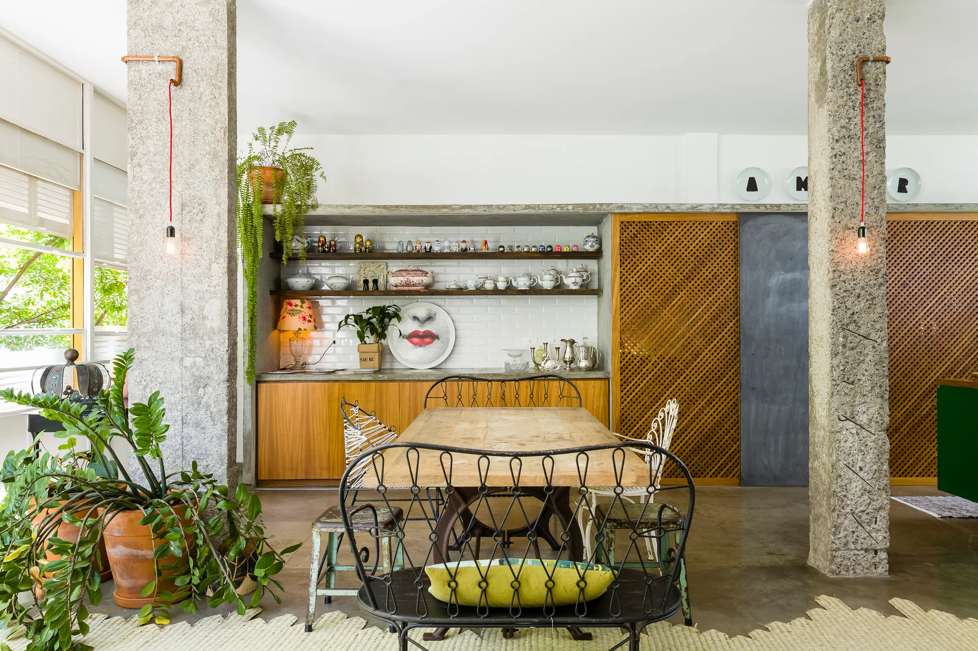 An eclectic dining room featuring a wooden table, mixed vintage chairs, two rough stone columns, and wood cabinets with lattice doors.