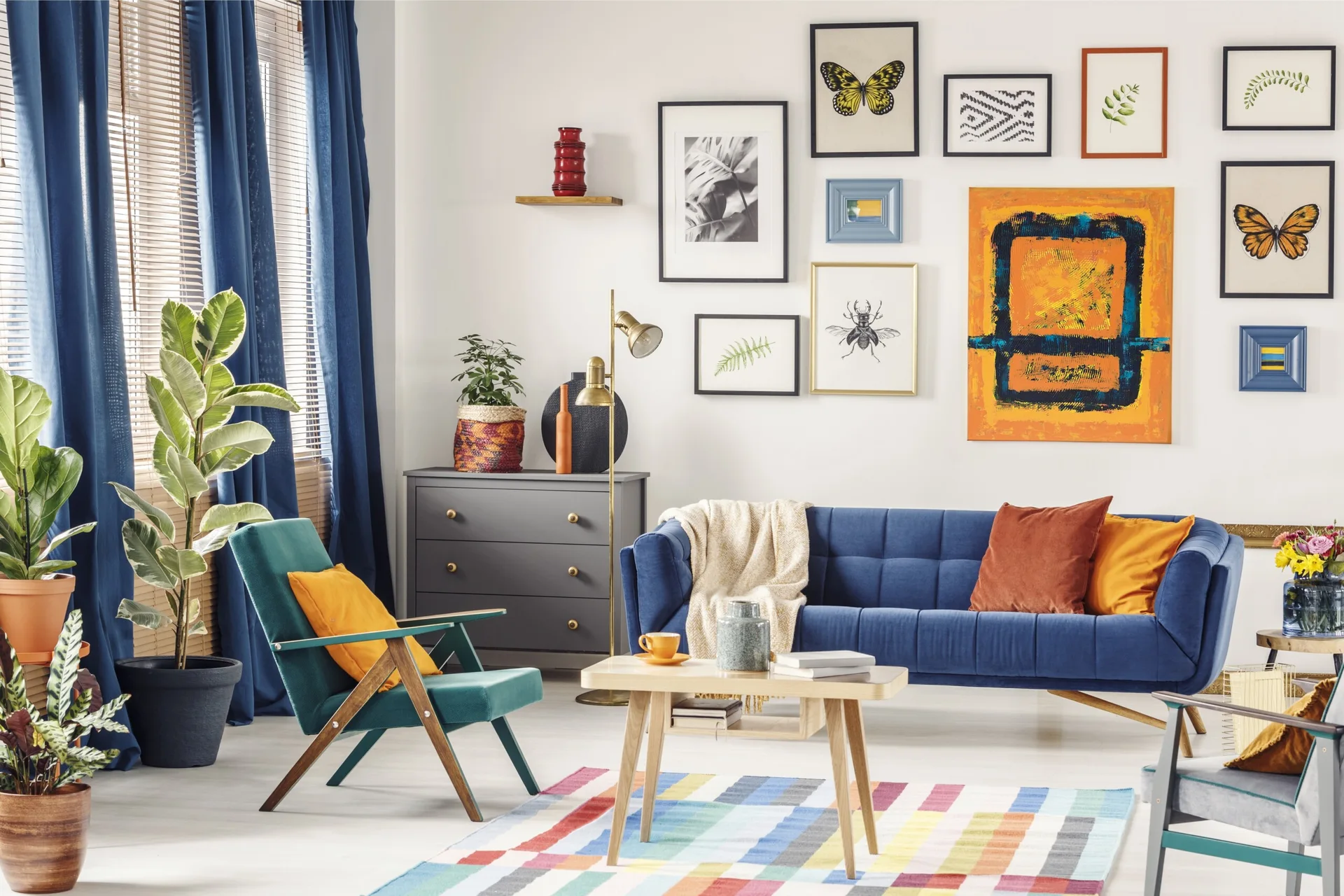 A colorful living room features a blue tufted sofa, a wooden coffee table, a teal armchair, and an eclectic gallery wall.