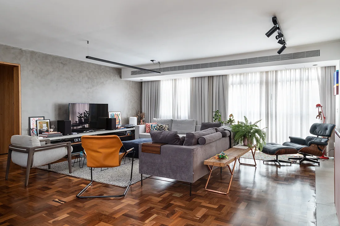 A living room features a textured concrete wall, wood parquet flooring, a gray sectional sofa, and mid-century modern accent chairs.