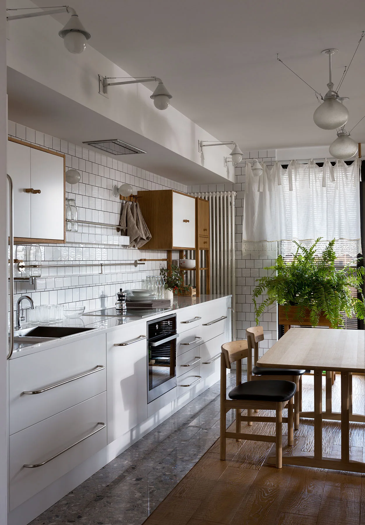 Modern kitchen and dining space featuring white subway tile walls, white cabinetry, a wood table, and a stone to wood flooring transition.