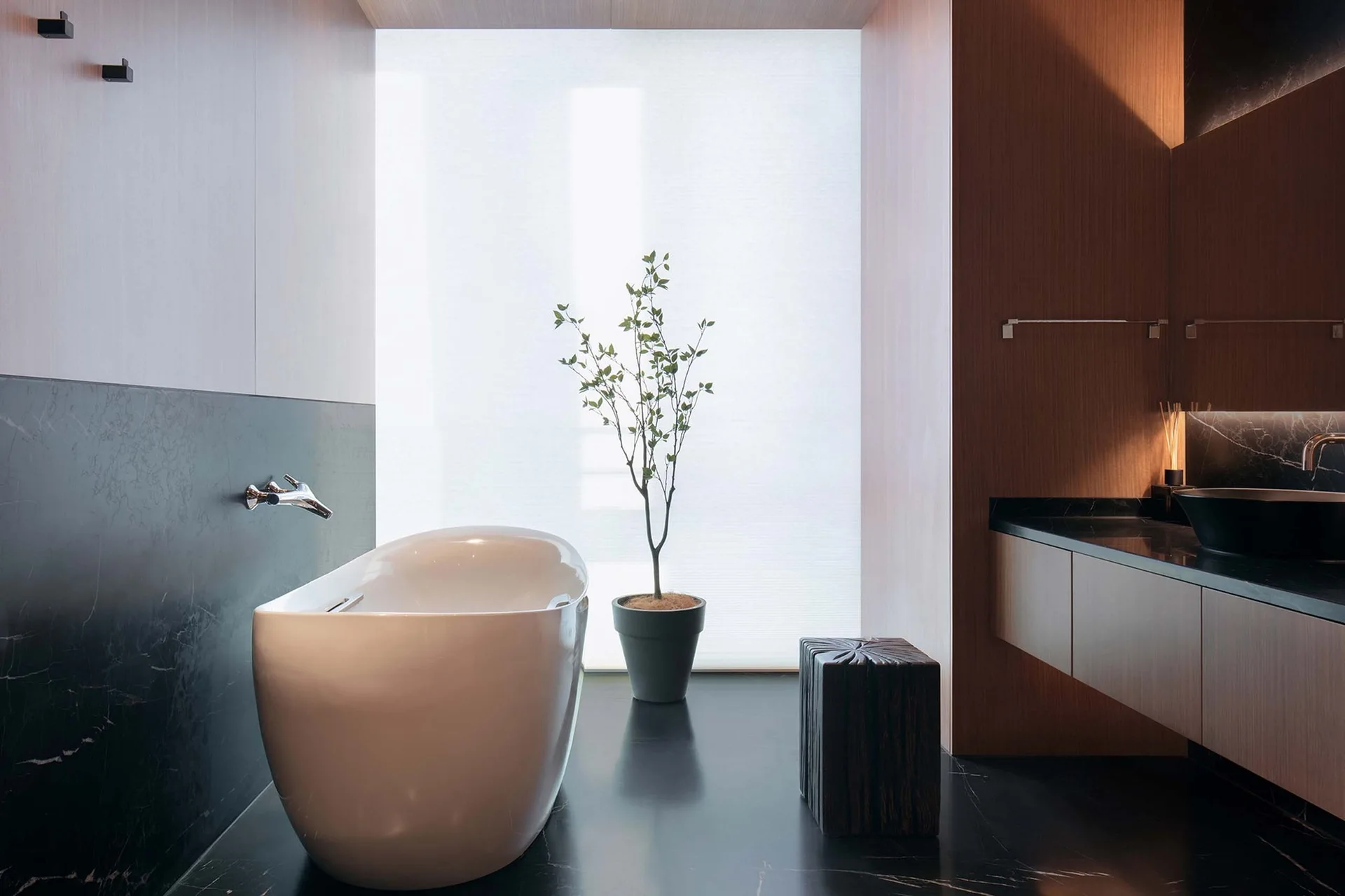 A modern bathroom features a white freestanding bathtub on black stone flooring, adjacent to a wooden vanity and a large frosted window.