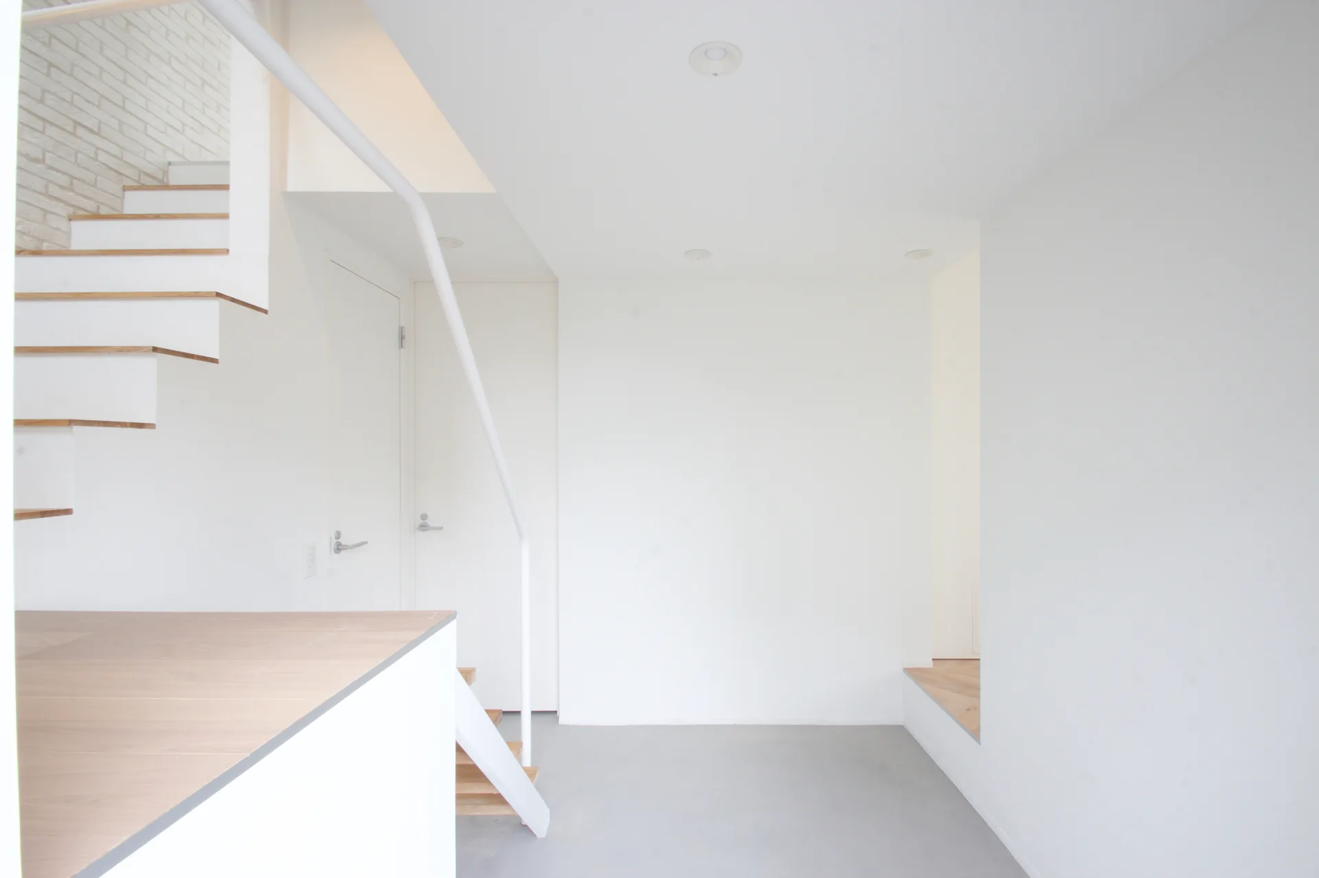 A minimalist white staircase features open-riser wood treads and a white metal handrail next to matching flush doors on a light gray floor.