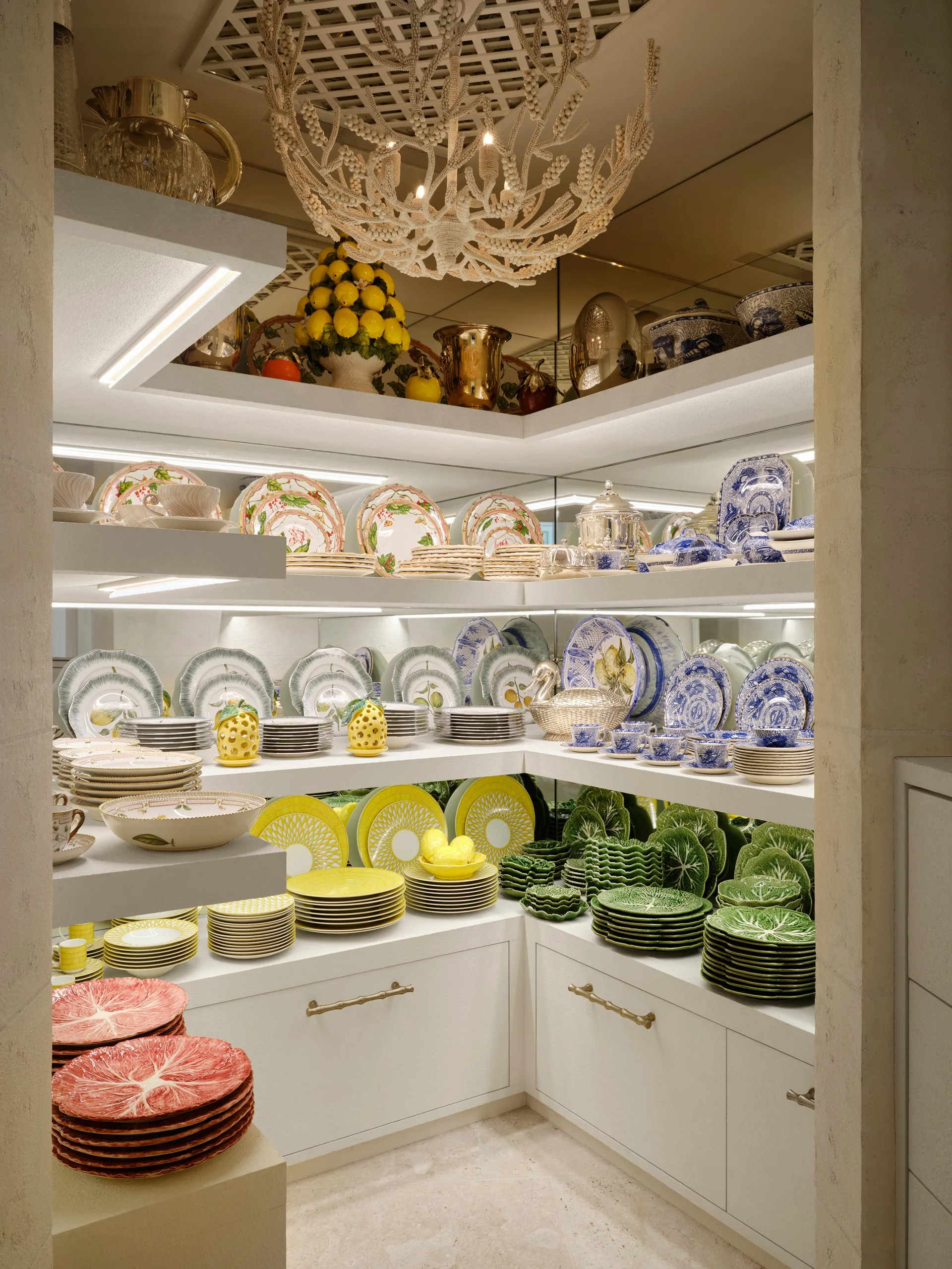 White L-shaped built-in shelves display colorful dinnerware collections, illuminated by under-shelf lights against a mirrored backing.