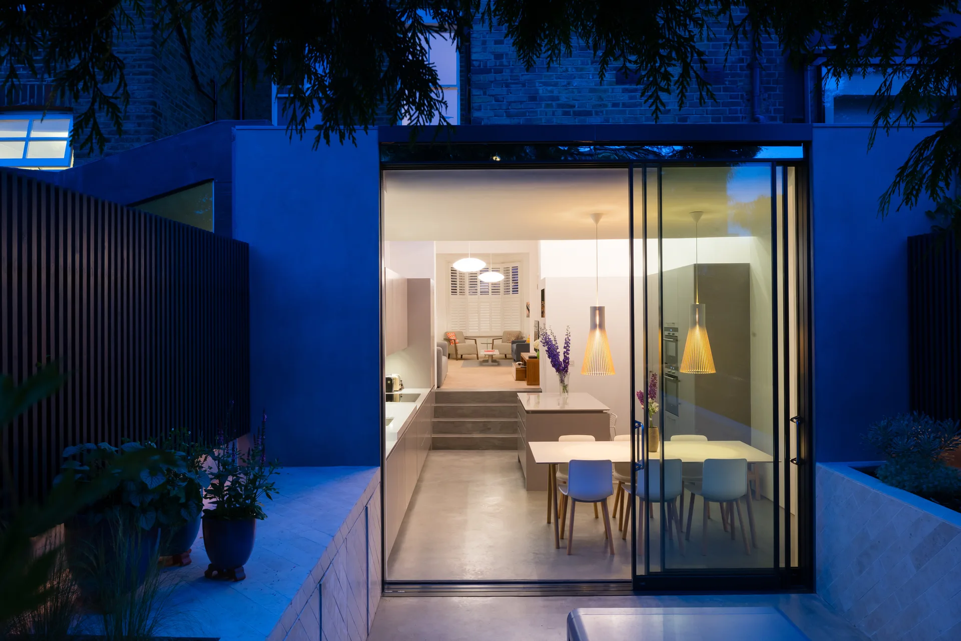 A view from the patio into a modern split-level kitchen and dining room with a concrete floor, steps, and sliding glass doors.