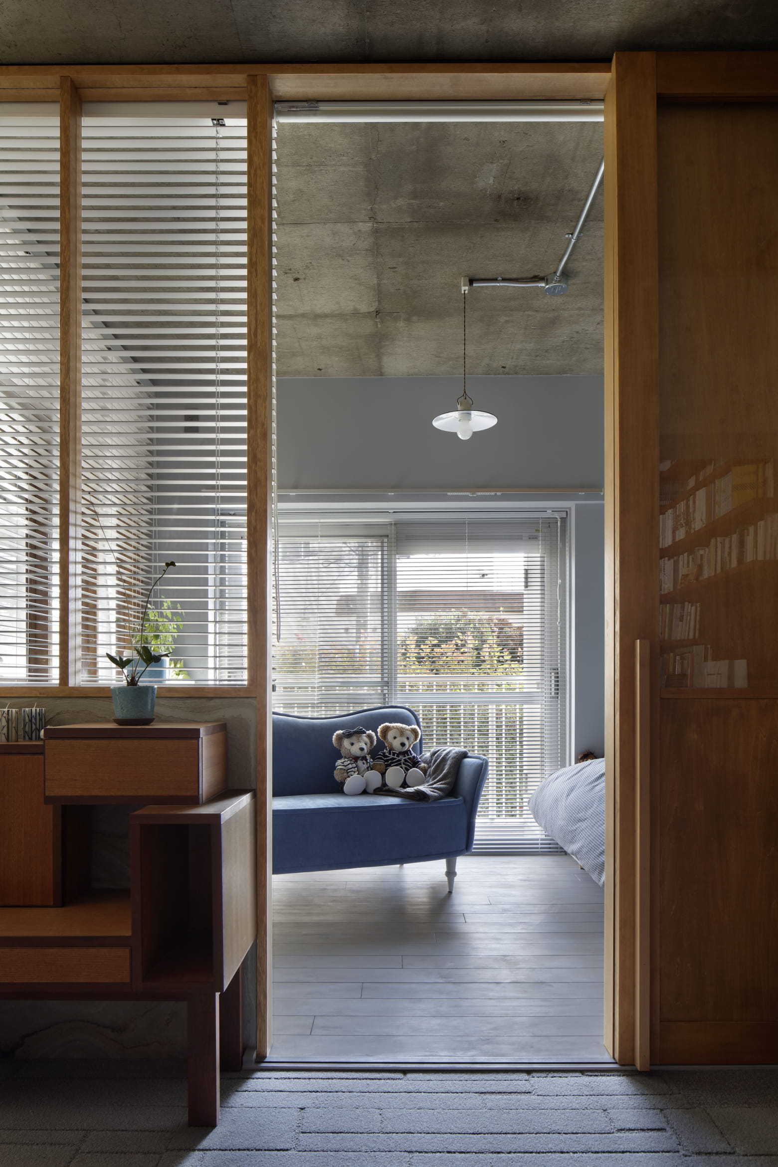 A wooden framed glass partition opens to a room featuring a blue sofa, raw concrete ceiling, and light wood floors.