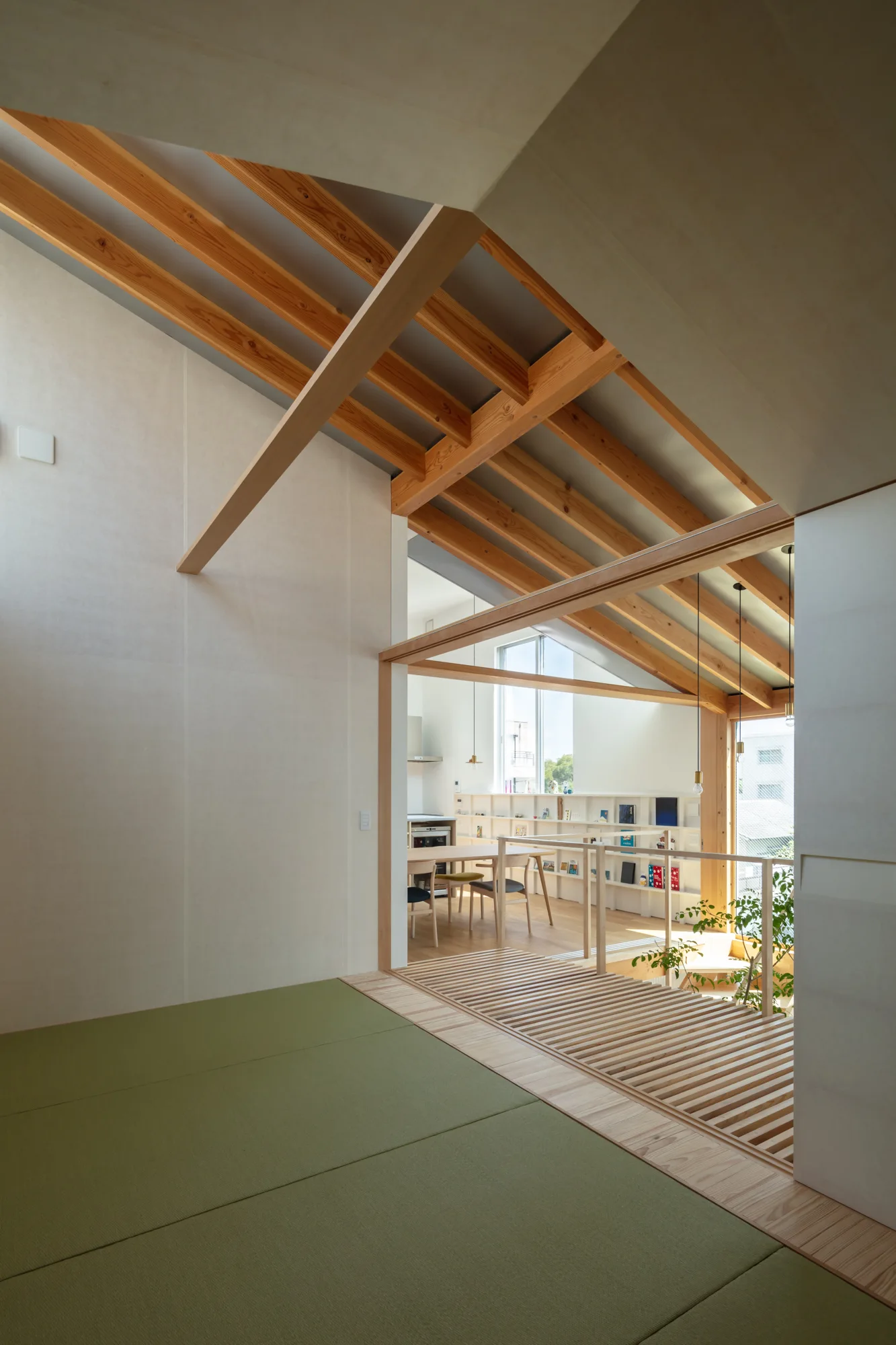 An open-plan interior featuring green tatami mats in the foreground, a wooden slatted floor transition, and exposed timber rafters on a pitched ceiling.