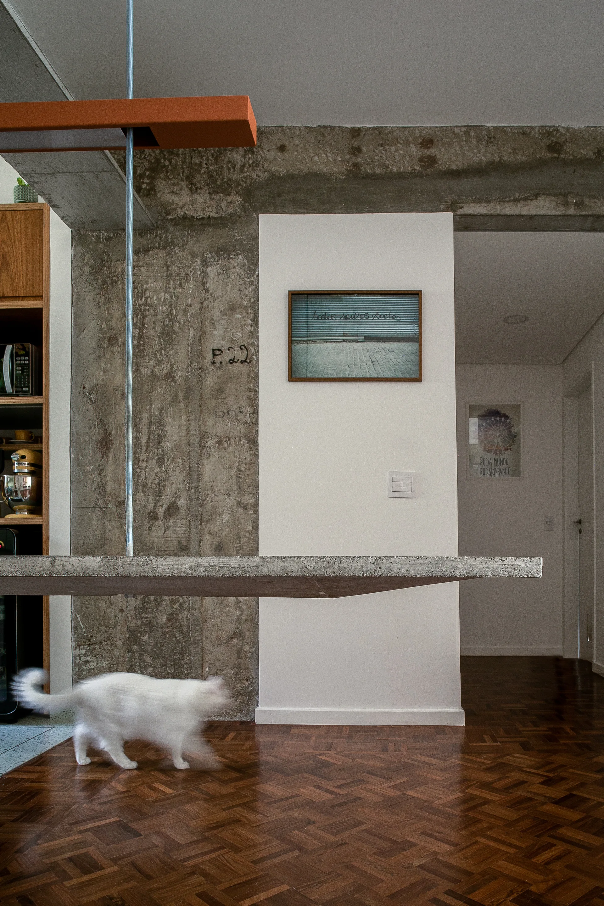 A suspended concrete countertop hangs in a modern industrial home featuring a raw concrete column, white walls, and dark parquet wood flooring.