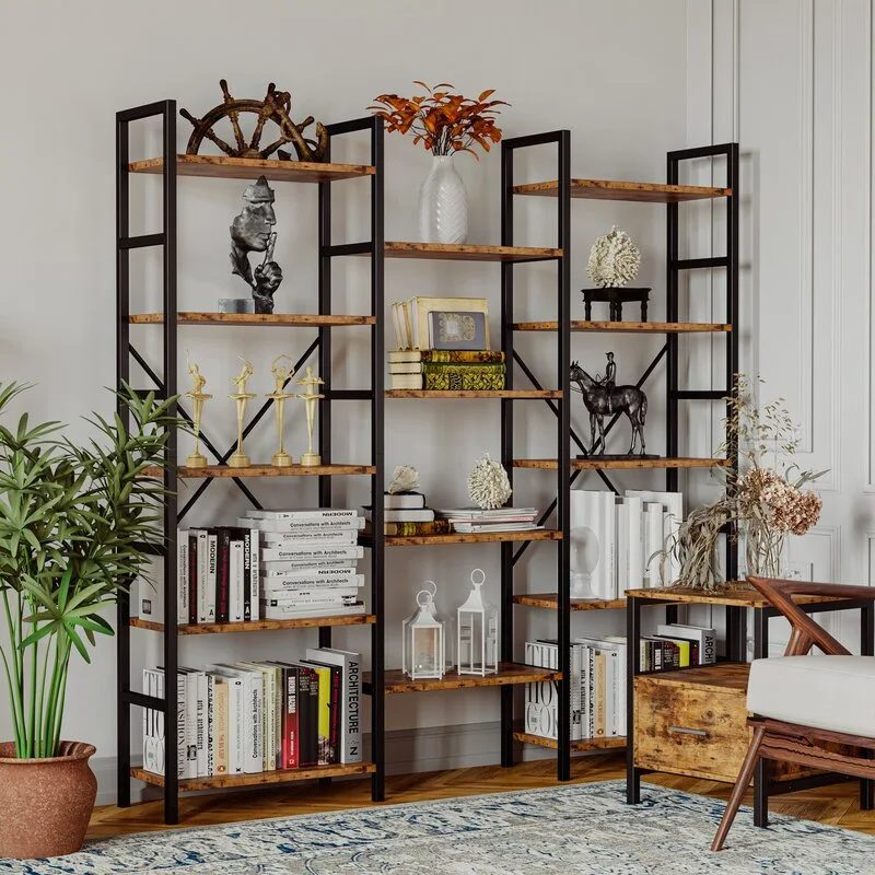 An industrial black metal and wood bookshelf is styled with books and sculptures next to a matching side table and a large green plant.