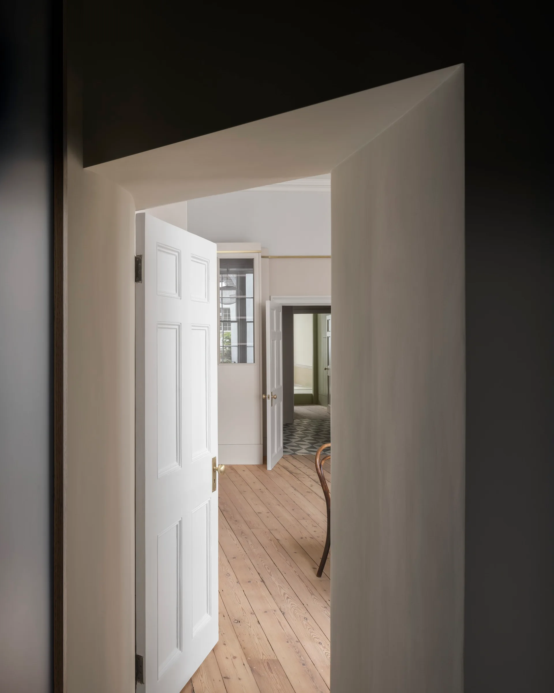 A perspective view through multiple open white paneled doorways showing wooden floors, plaster walls, and a tiled room in the distance.