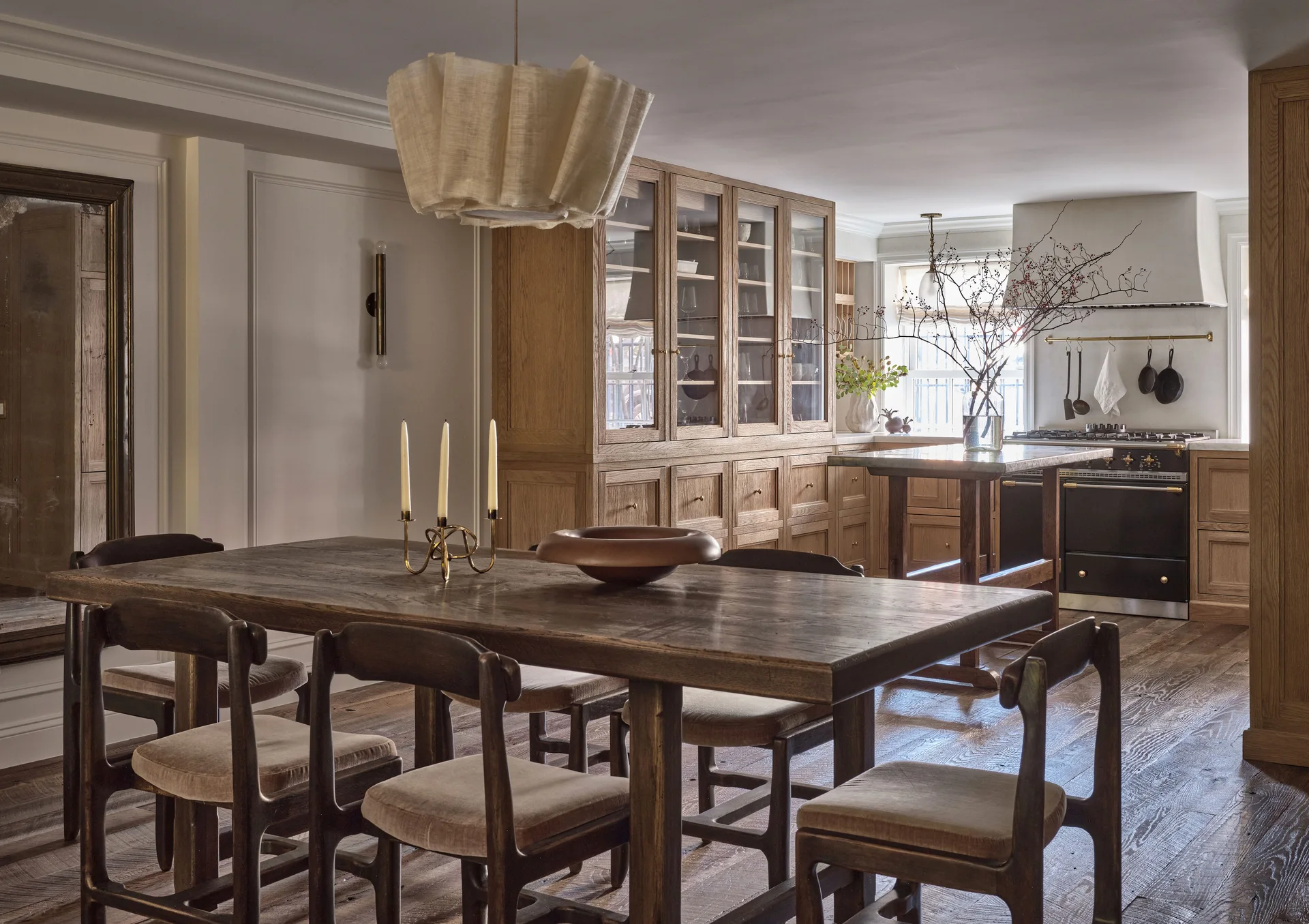 A dining and kitchen area featuring a dark wood dining table with chairs, light oak cabinets, and a pleated pendant light.