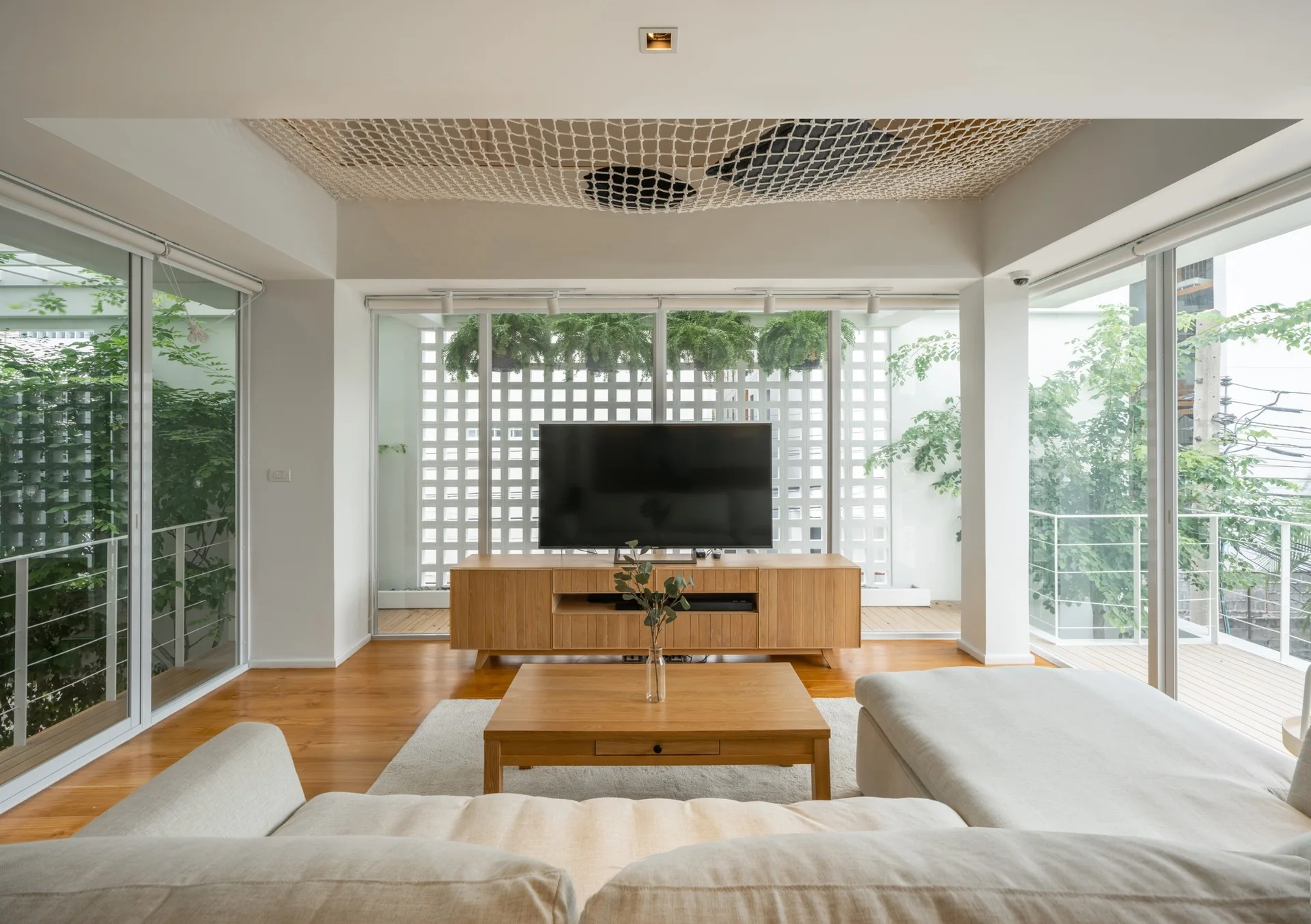 A modern living room featuring a light beige sectional sofa, a wooden coffee table, and a TV console in front of sliding glass balcony doors.
