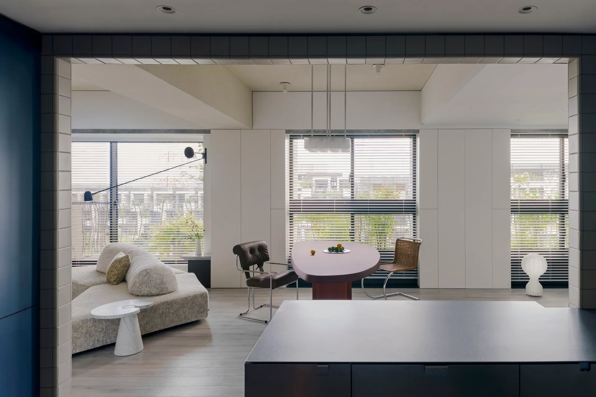 A modern open-plan living room featuring a curved grey fabric sofa, an asymmetric wooden dining table, and mismatched cantilever chairs.