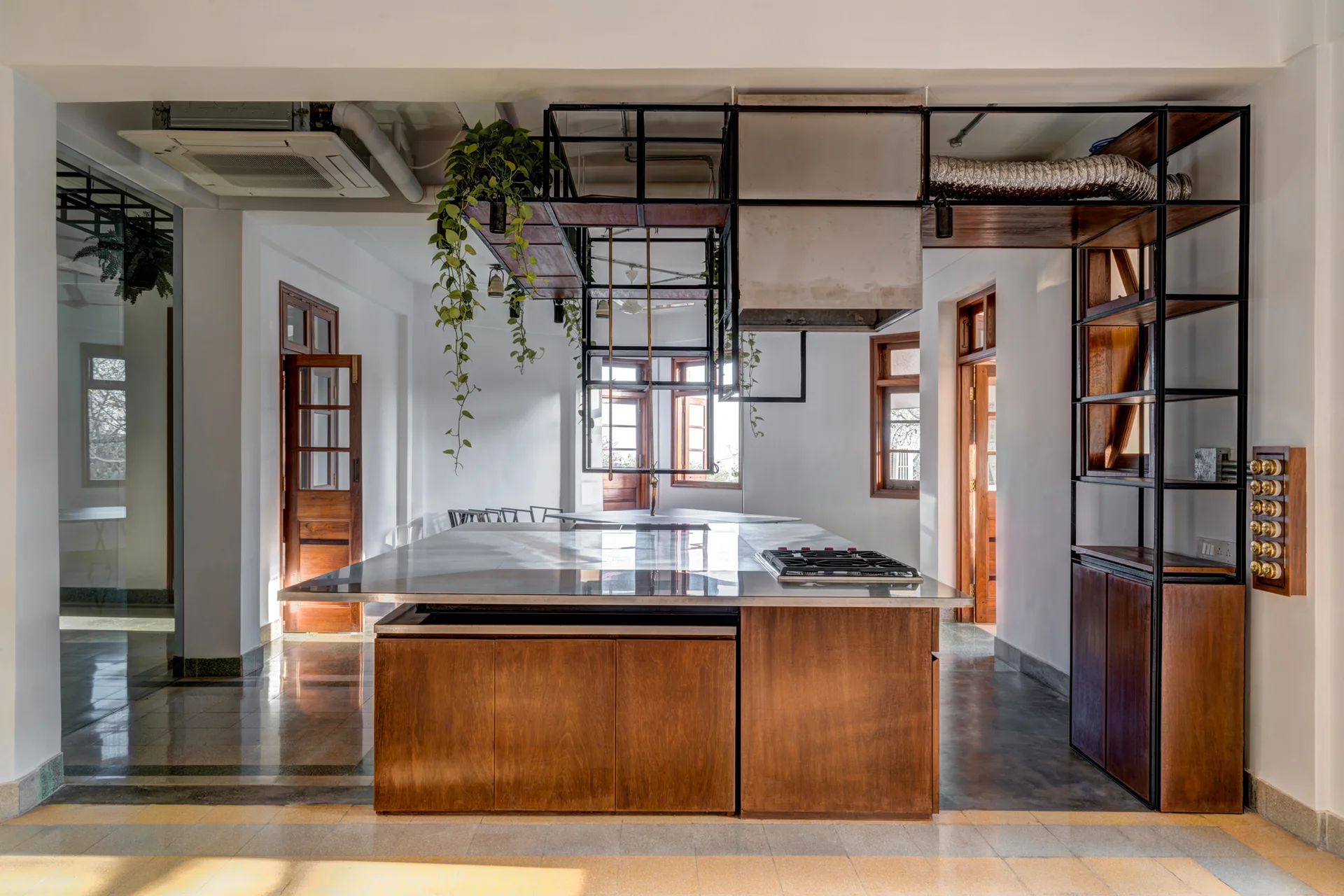A spacious kitchen features a central wood-base island with a metal countertop beneath a suspended black metal rack and open shelving.