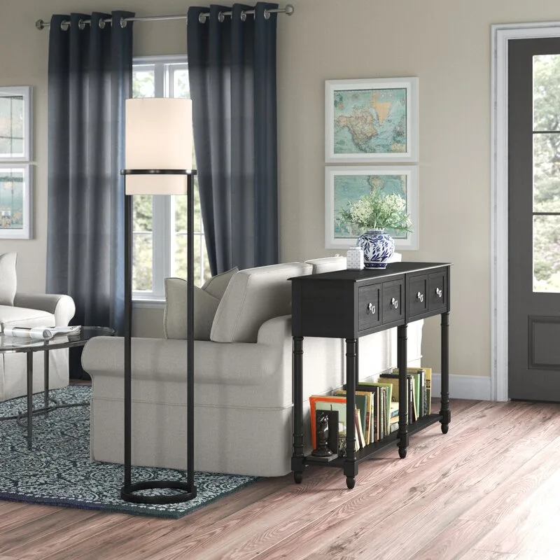 A beige sofa is paired with a narrow black wooden console table holding books and a blue vase, set against a blue-patterned rug.