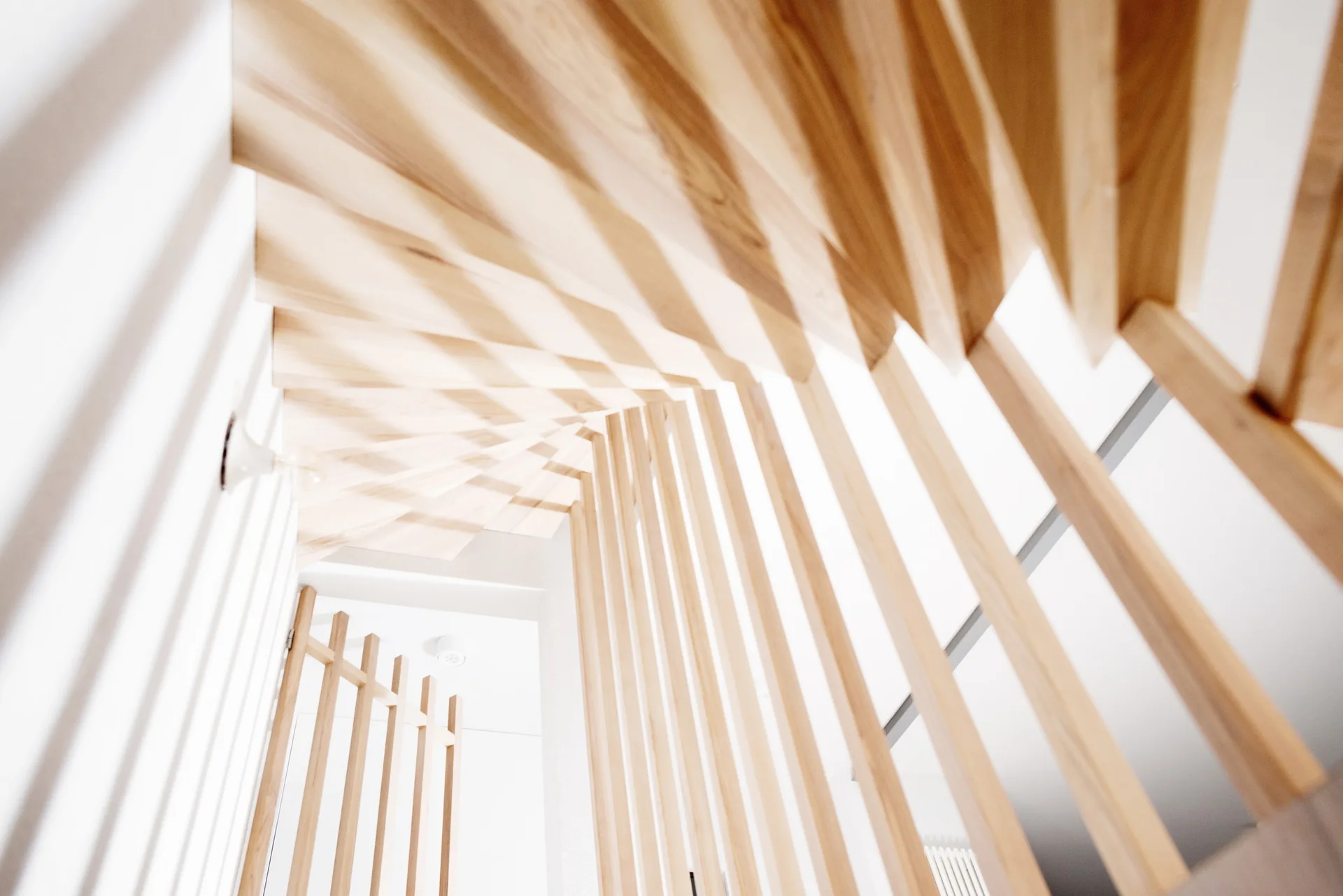 Upward perspective of a modern staircase featuring light wood treads and a vertical timber slat screen against white walls.