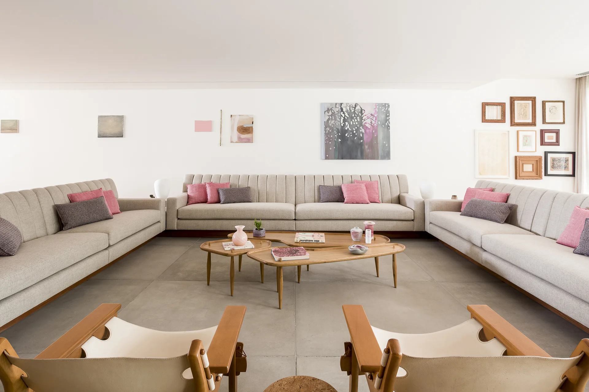 A spacious living room features a U-shaped arrangement of cream sofas surrounding three nested wooden coffee tables on large grey floor tiles.