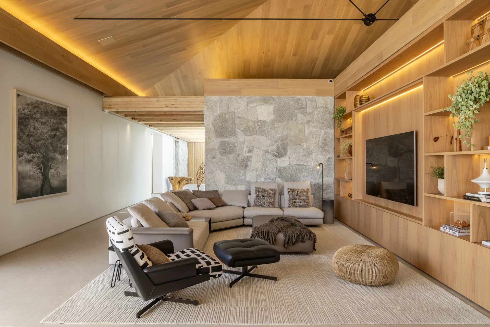 A modern living room features a vaulted wood ceiling, a large stone accent wall, a light gray sectional sofa, and custom wood built-in shelving.