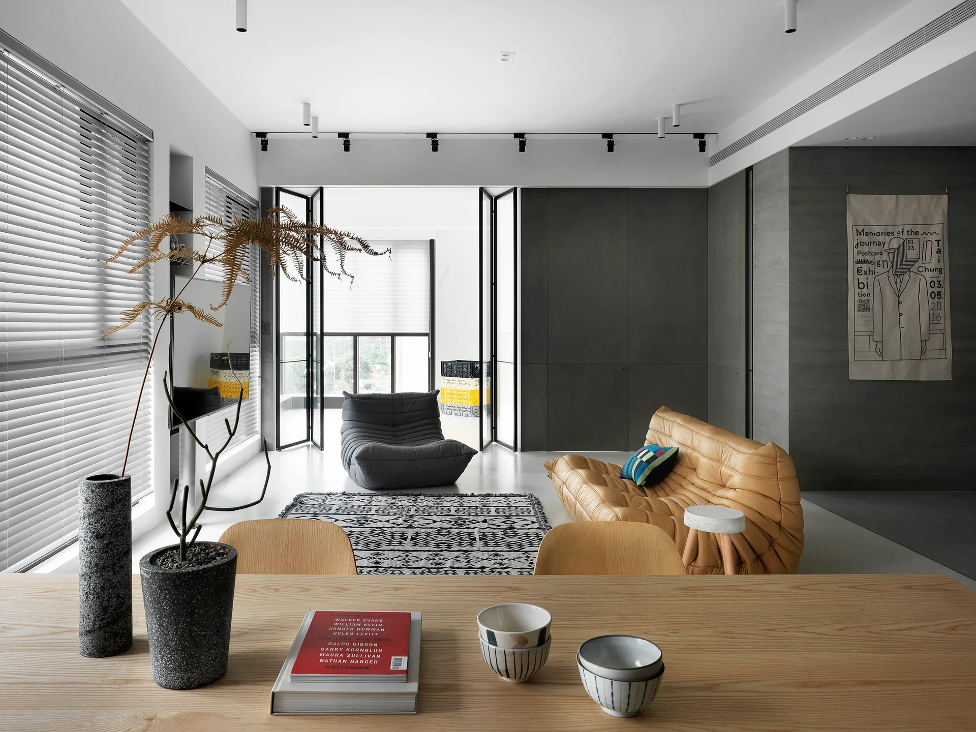 A modern minimalist living room features a tufted camel leather sofa, grey armchair, and geometric area rug in front of dark grey wall panels.