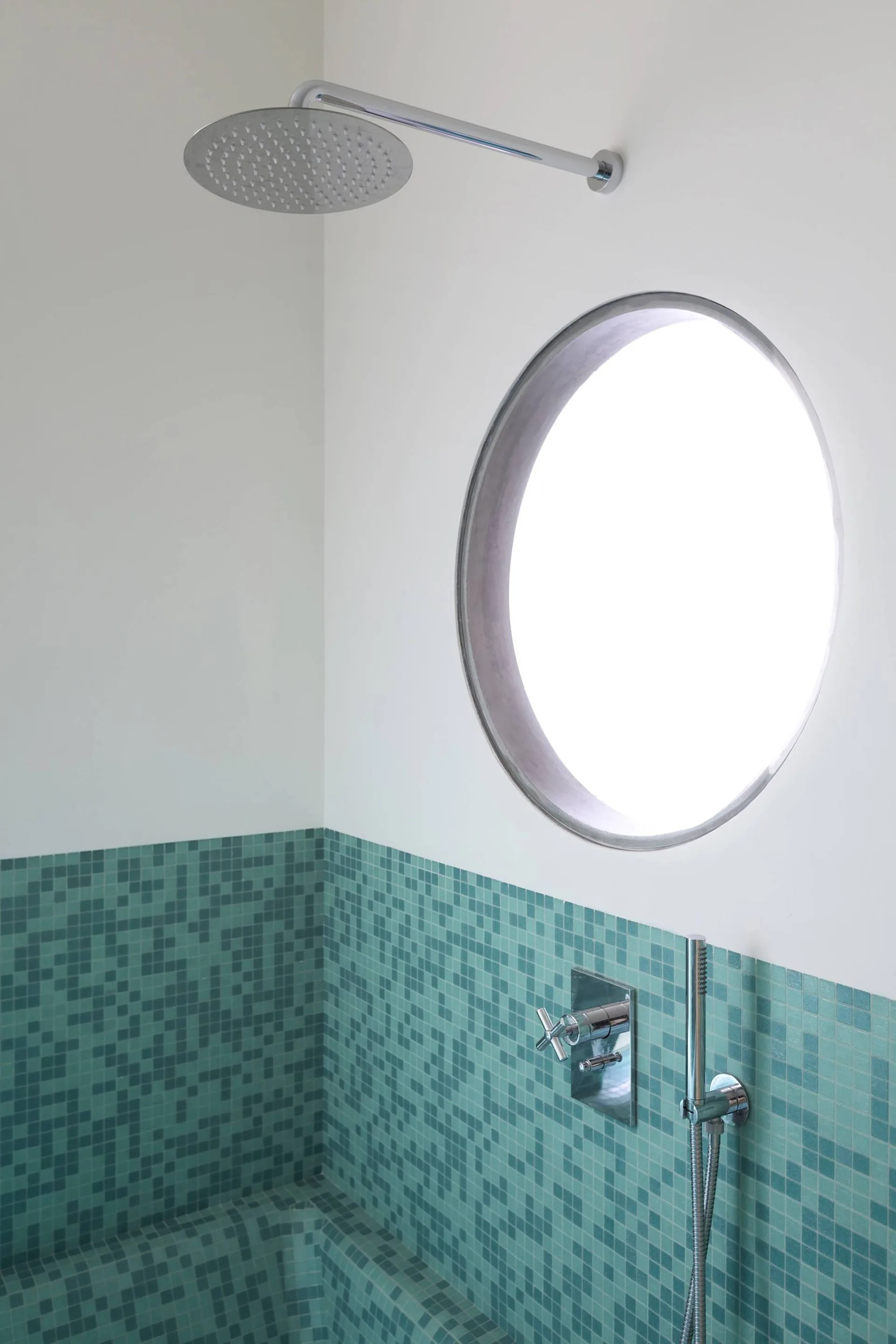 A modern shower features green mosaic wall tiles, a circular porthole window, and a wall-mounted chrome rainfall showerhead.