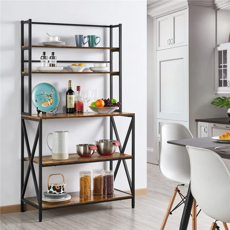 A tall industrial-style baker's rack with a black metal frame and wood-toned shelves holding dishes, jars, and kitchen supplies against a white wall.